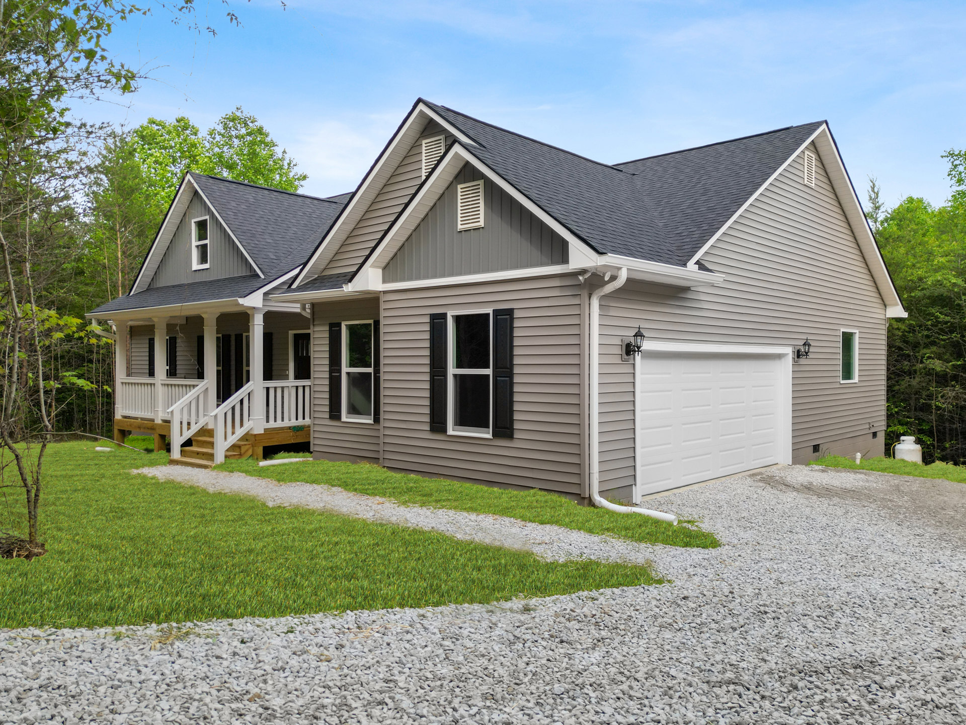 Two-story home with white garage door, lamp mounted beside entrance, gravel path along side, paved driveway, white-framed windows, gabled roof, mature trees, and Robert Frost Farm