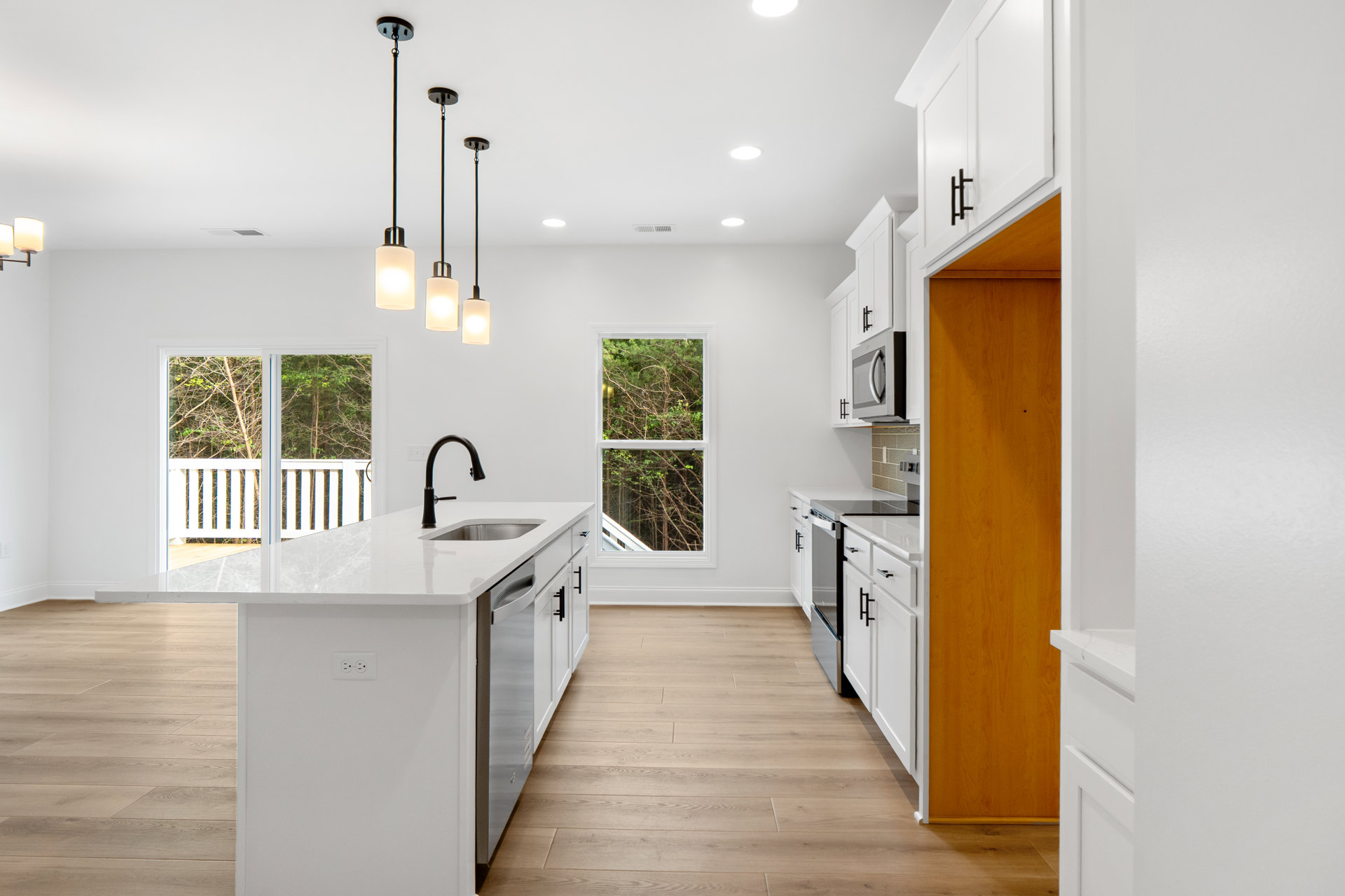 White kitchen cabinets, wood flooring, window with trees outside, wooden door with white frame, built-in microwave, ceiling light fixture