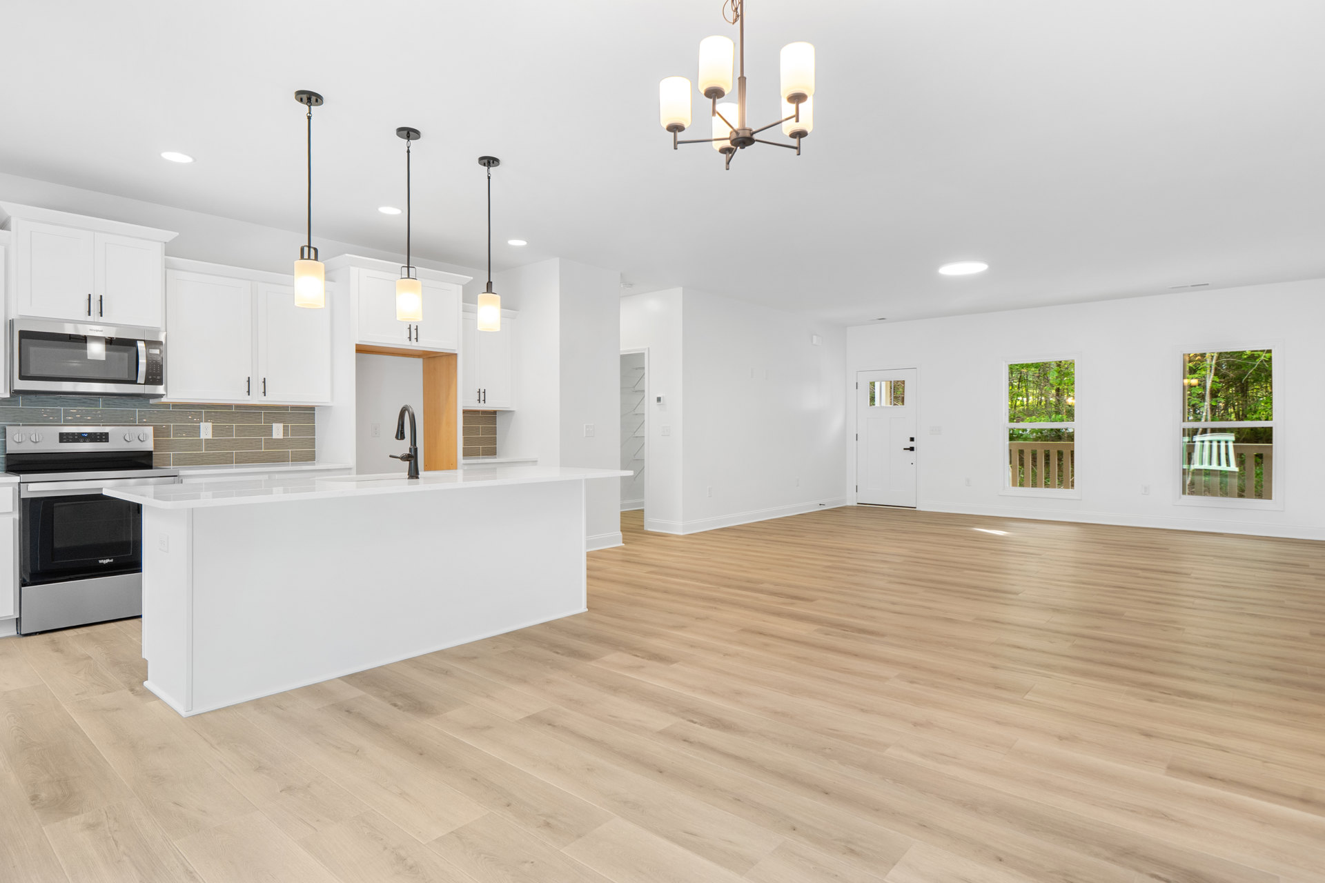 Kitchen with white walls, wood laminate flooring, white cabinetry and countertop, black faucet, built-in microwave, and a white chair visible outside the window