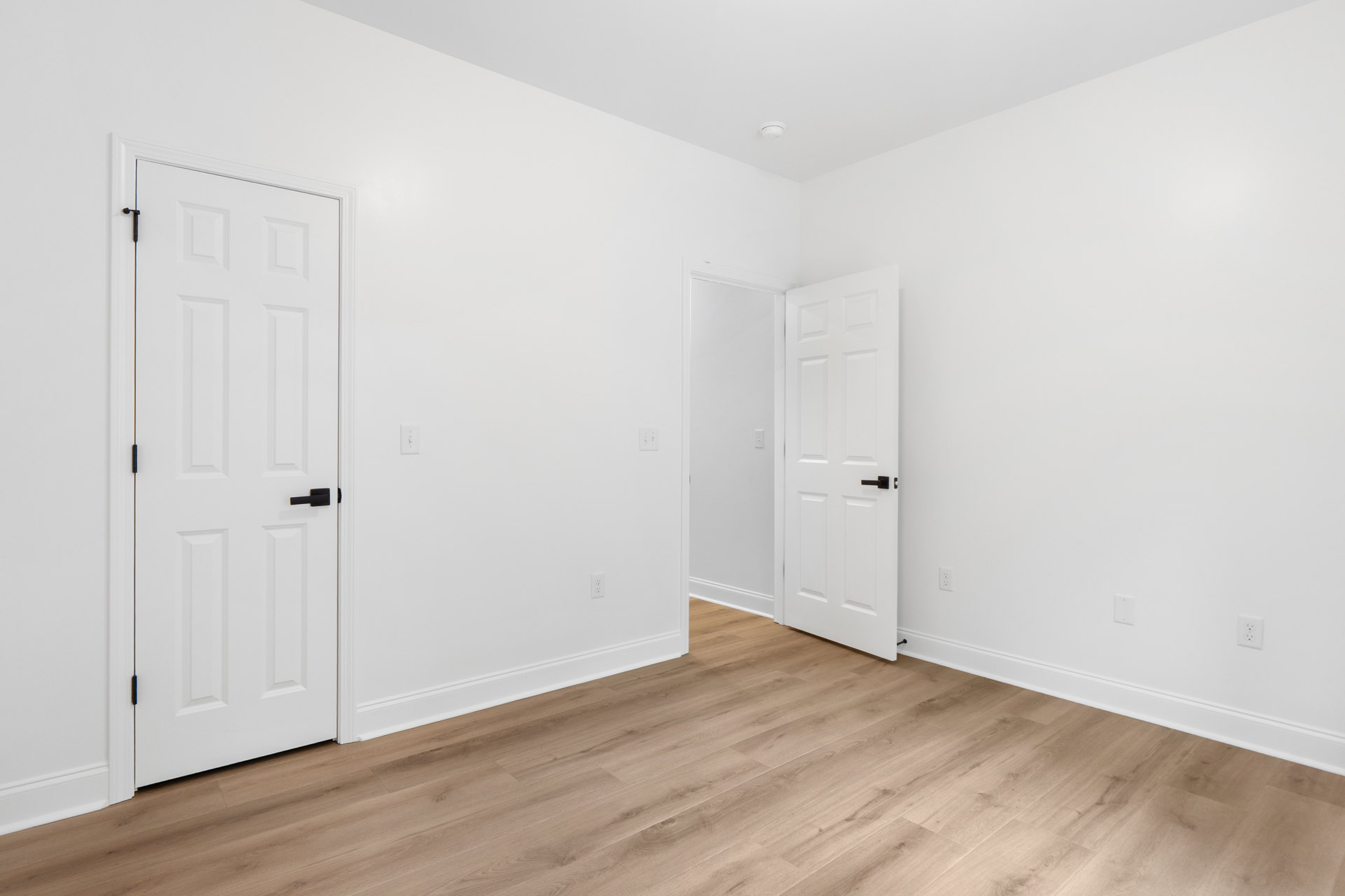White walls and ceiling, wood laminate flooring with white base trim, white door featuring a black handle