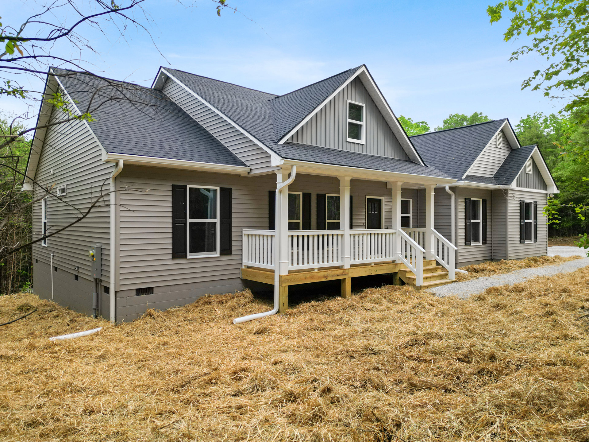 White house with a covered porch, black shuttered windows, white deck railing, and a yard covered in hay; Robert Frost Farm visible in the background.