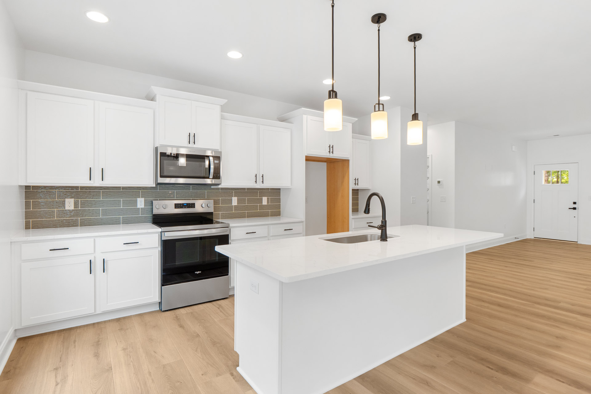 White kitchen featuring shaker cabinets, quartz island, black undermount sink, stainless steel stove with glass door, built-in microwave, pendant lighting, and hardwood flooring.