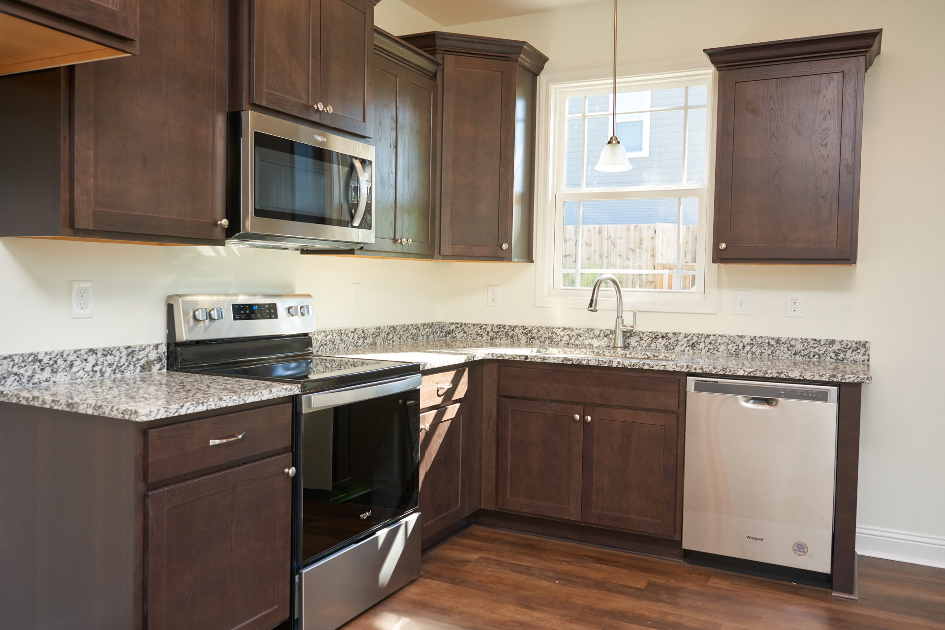 Kitchen with dark wood cabinets, granite countertops, open black microwave, stainless steel dishwasher with control buttons and sticker, close-up of ceiling light, brown cabinet
