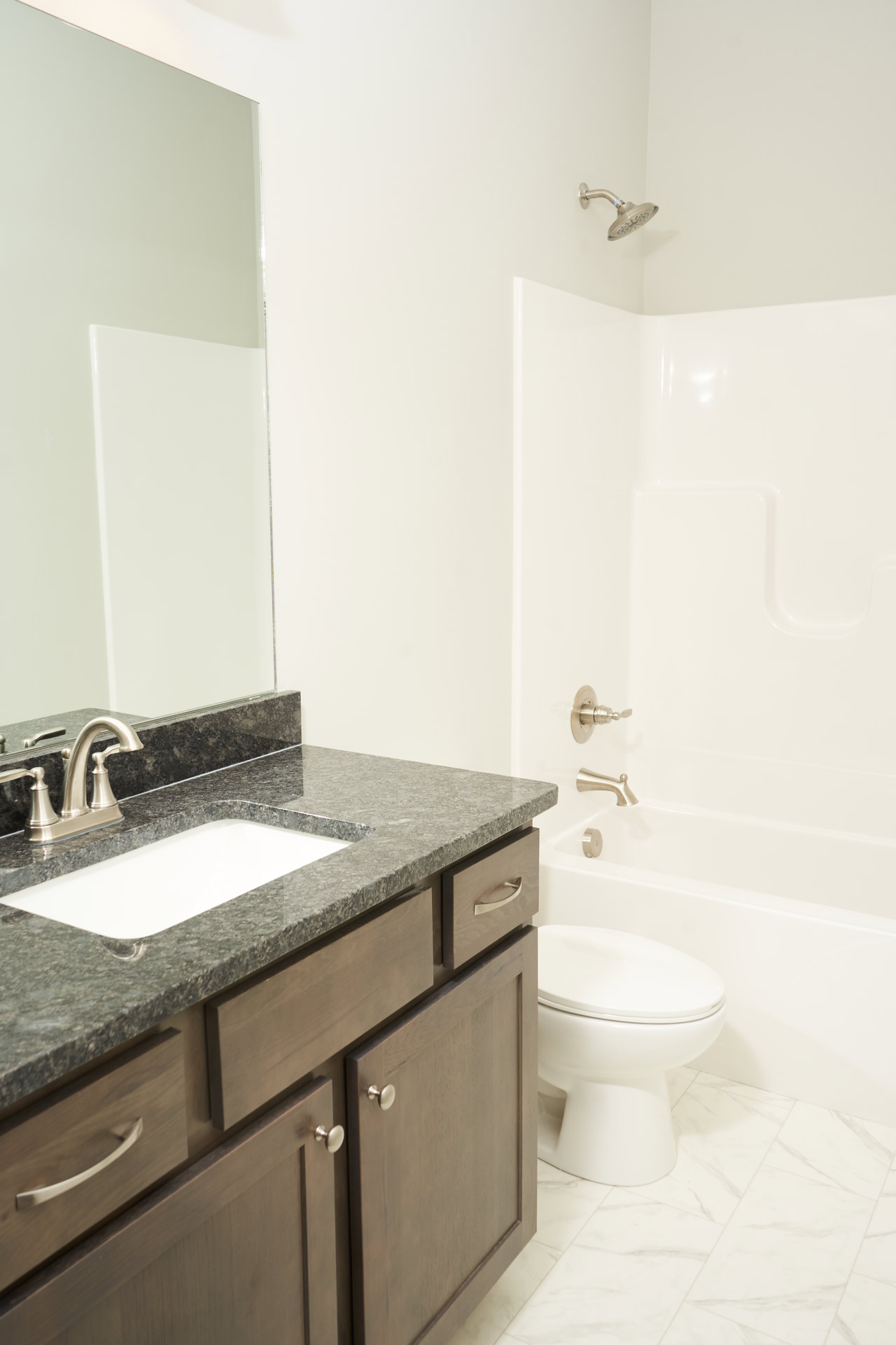 Modern bathroom featuring white ceramic sink with silver faucet, matching white toilet, tiled walls, and chrome shower head.