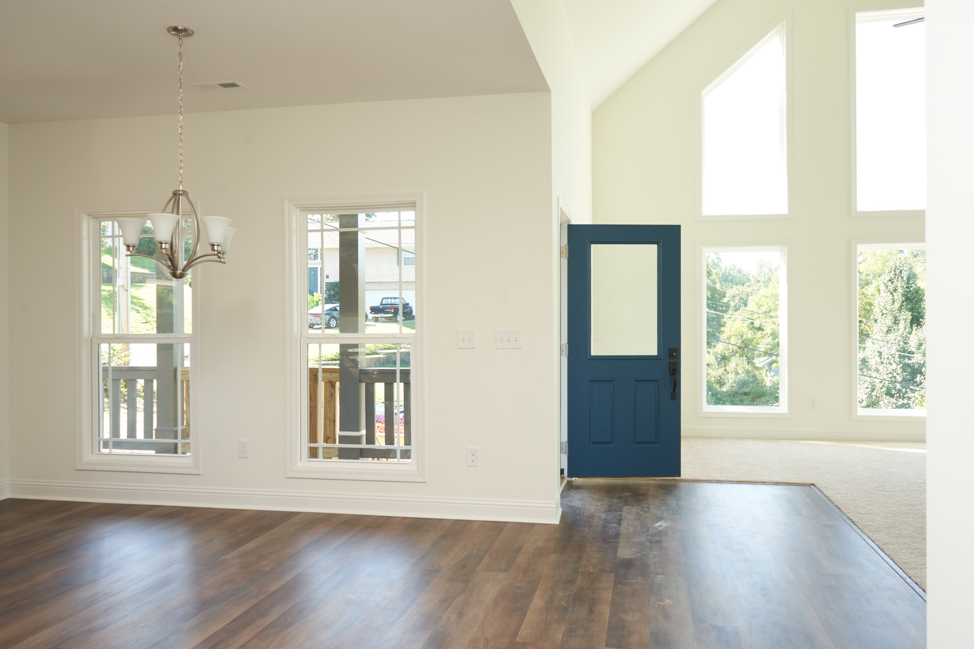 Wood floor with white baseboard, blue door featuring glass panel, window showing trees outside, black truck visible in driveway, lamp blurred in foreground