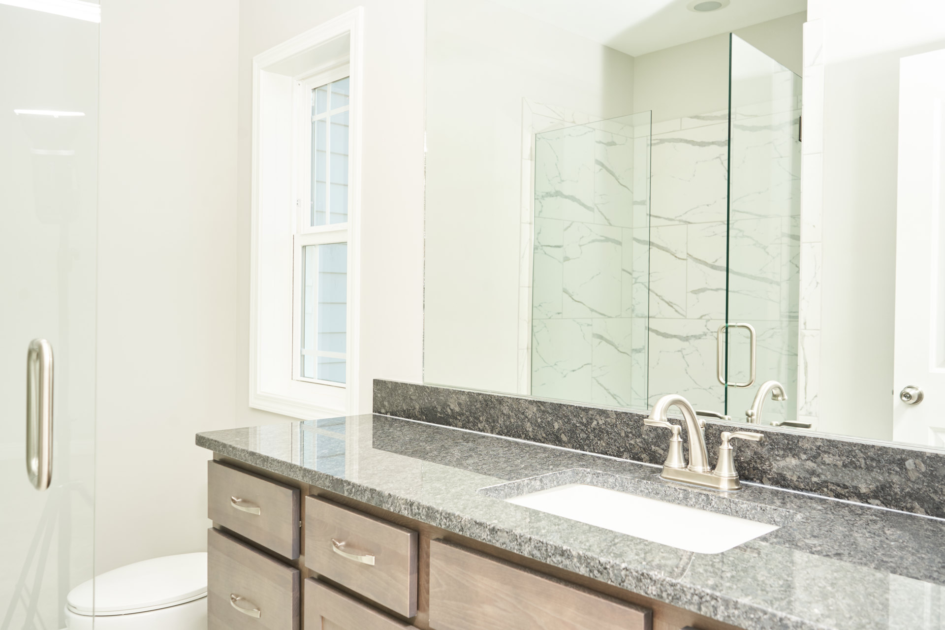 Bathroom with marble countertop, undermount sink, chrome faucet, glass-enclosed shower, and large wall mirror