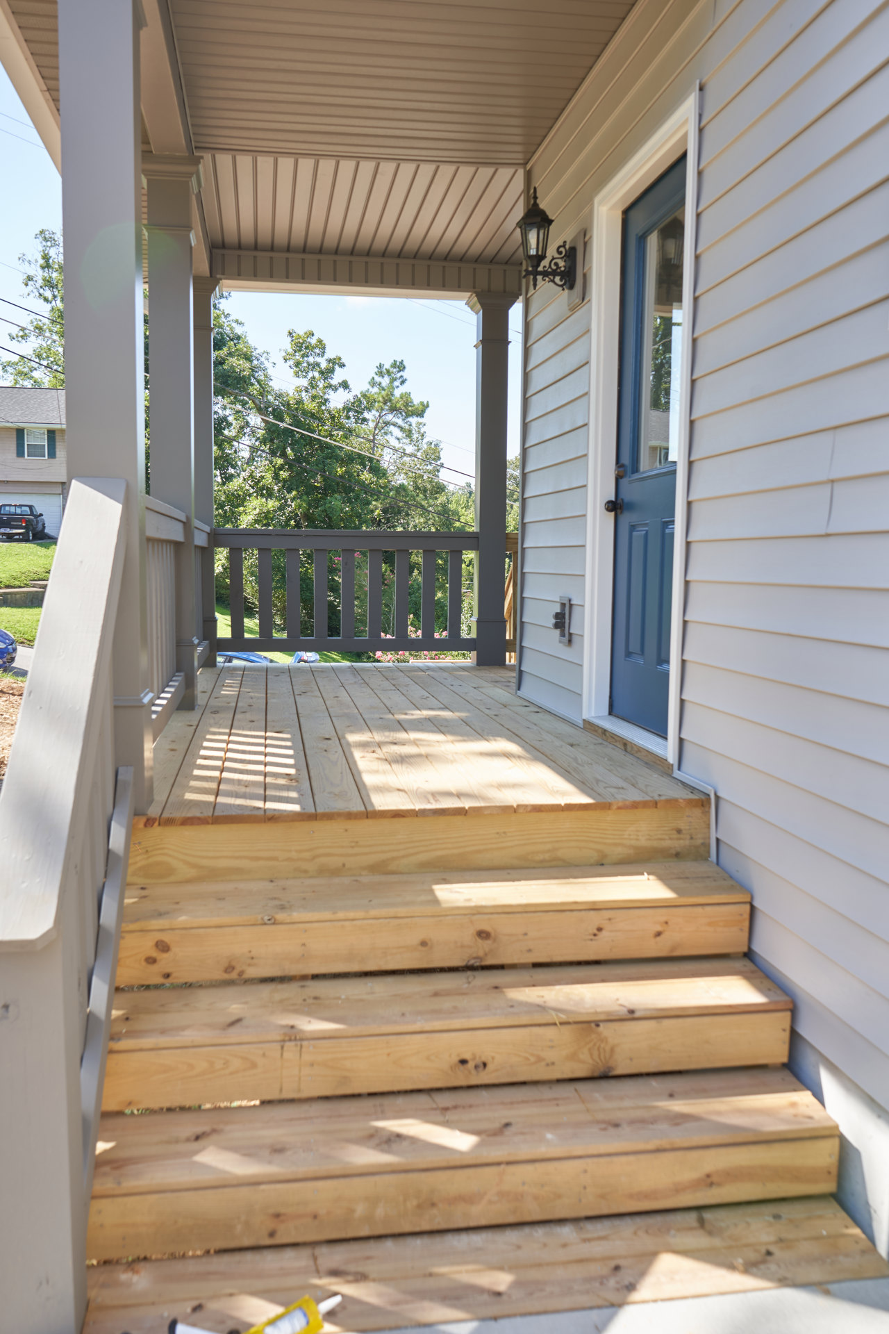 Wooden exterior staircase with railing leading to a porch, black truck parked beside the house, balcony overlooking trees and power lines, lamp post with exposed bulb, wood siding
