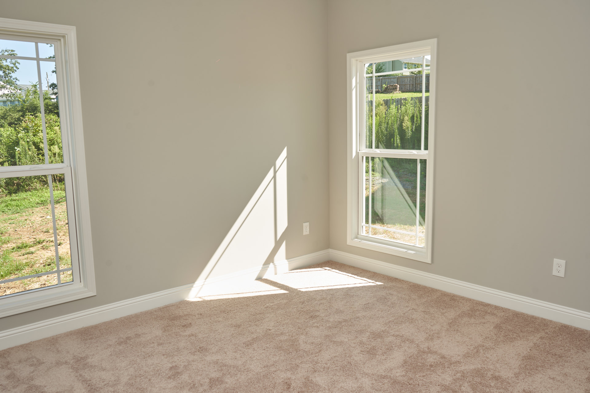Bedroom with light-colored carpet, white-framed window overlooking greenery, plaster walls, and natural daylight.