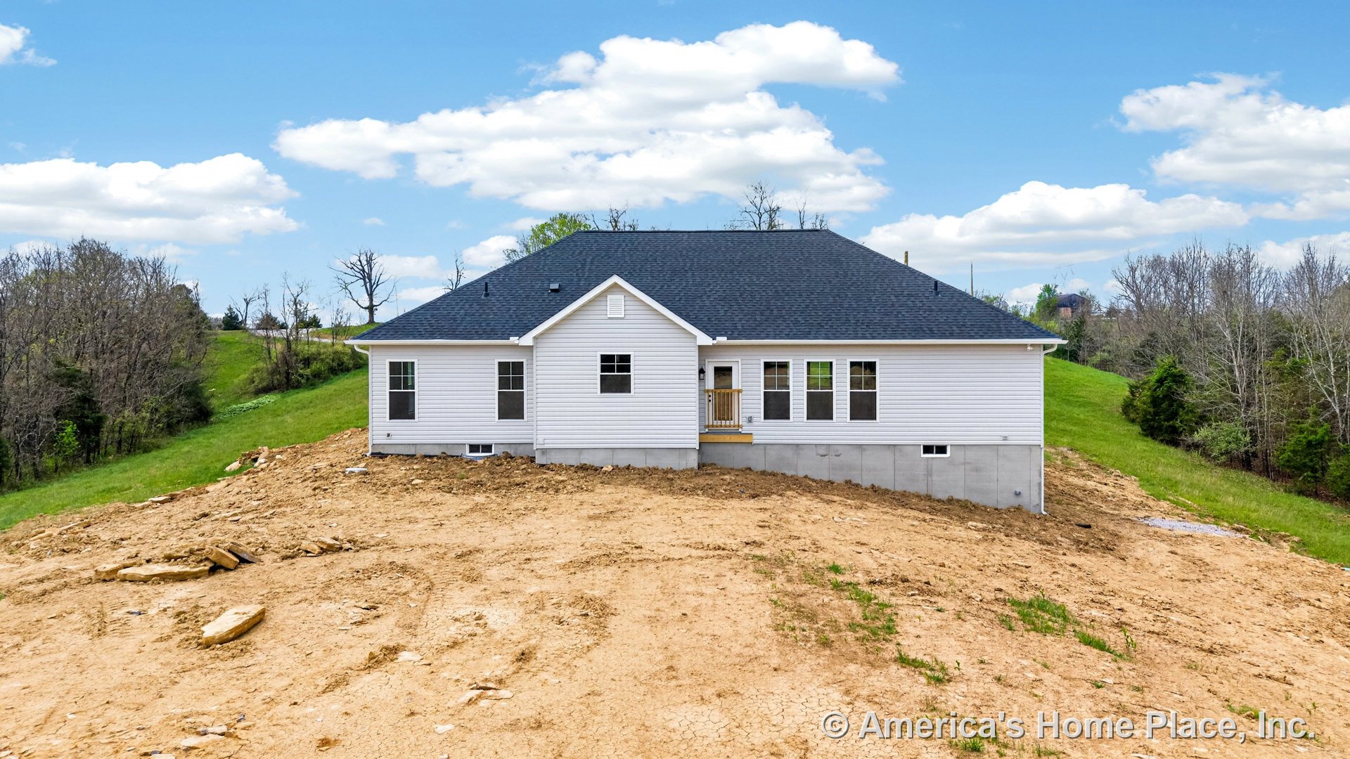 White vinyl siding exterior with black shingle roof, multiple rear windows, elevated porch featuring wooden railing, concrete foundation, and single-story layout.