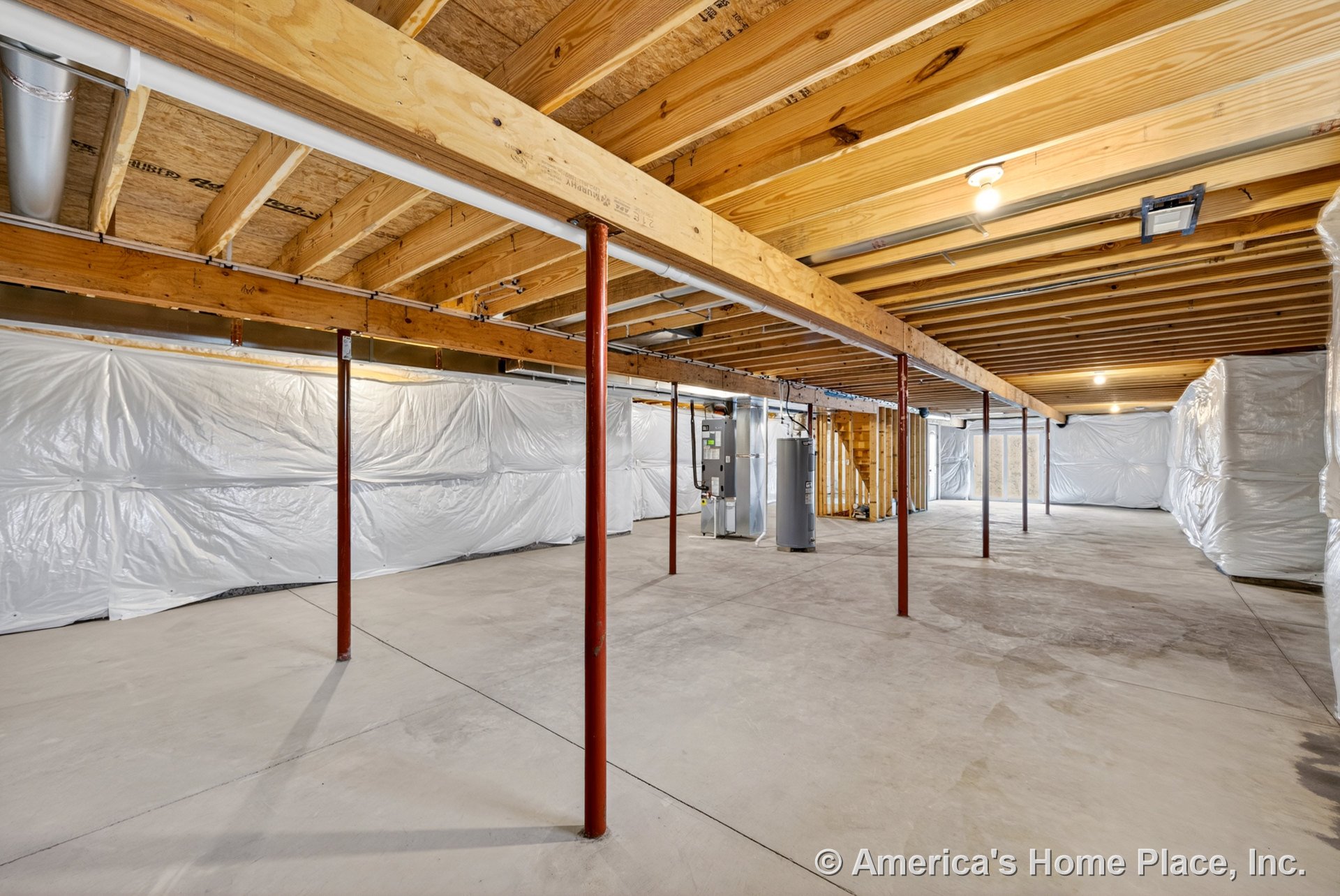 Unfinished basement with exposed wood ceiling joists, concrete slab floor, metal support columns, plastic-wrapped insulation on walls, utility area featuring a water heater, bare