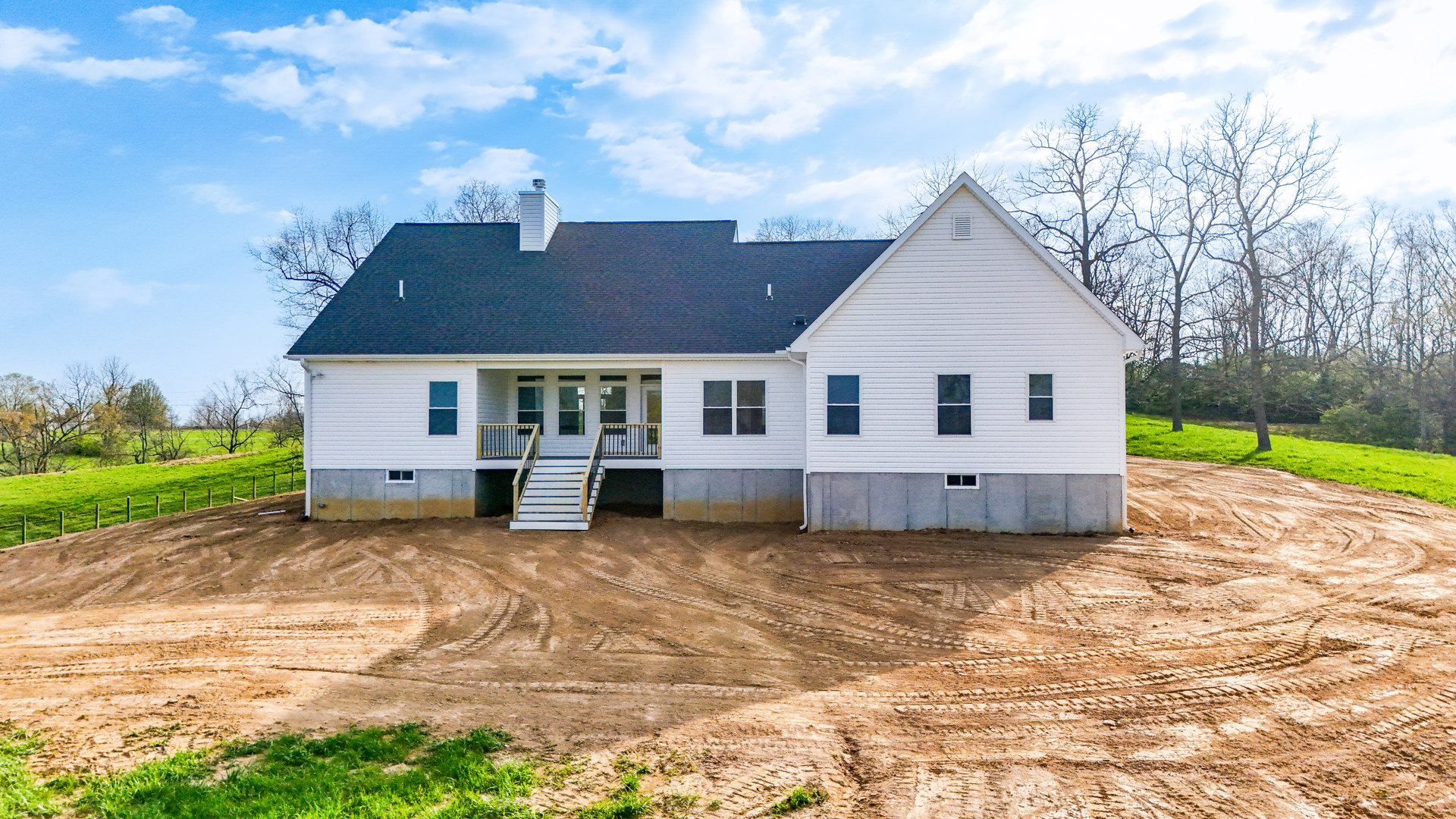White two-story cottage with white stairs and porch, white chimney topped with a cross, dirt yard, white-framed windows, and metal railing.