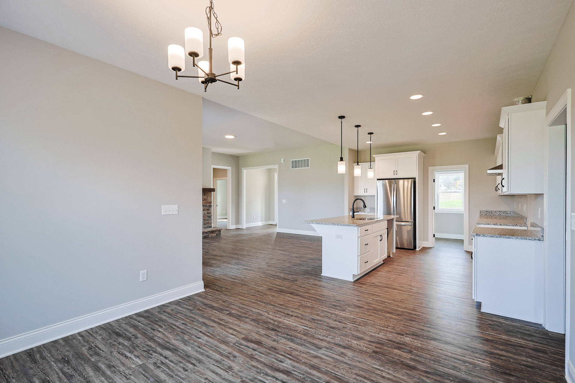 Open kitchen and dining area featuring wood flooring, white walls, a kitchen island with built-in sink and black faucet, stainless steel refrigerator, and modern ceiling fixtures.
