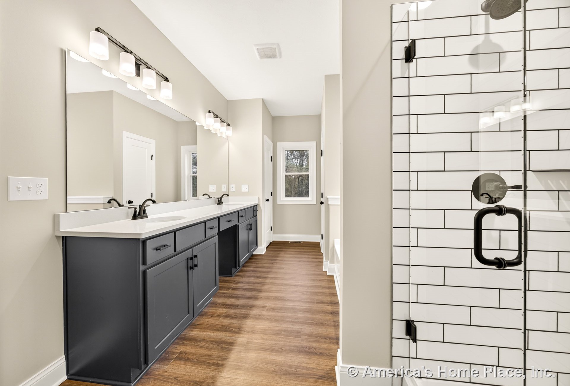 Double vanity with dark shaker cabinets and quartz countertop, glass-enclosed shower with white subway tile, wood-look flooring, large mirror, built-in lighting, matte black