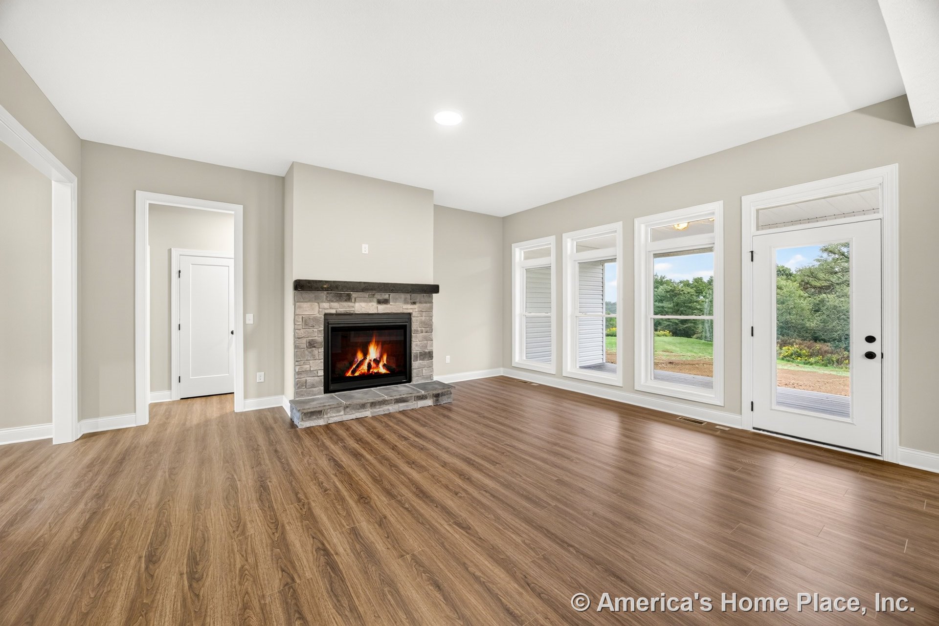 Stone surround fireplace with three tall windows and glass exterior door, wood-look plank flooring, white trim and baseboards, neutral wall color, ceiling light, and open layout