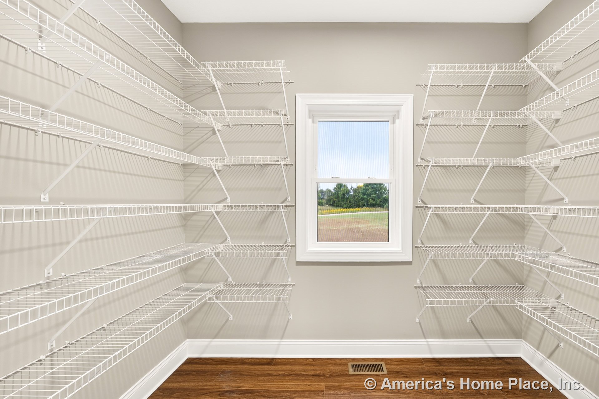 Walk-in pantry with multiple white wire shelves, single window framed in white trim, wood-look flooring, neutral painted walls, and baseboard trim.