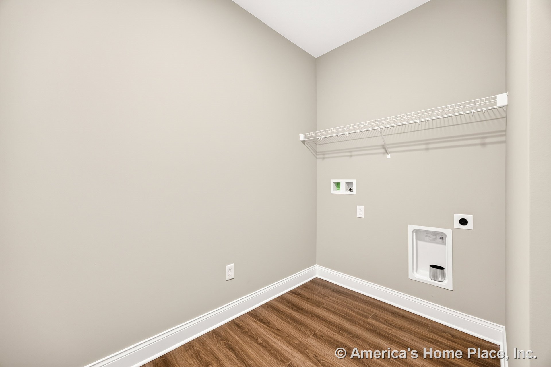 Utility room with wall-mounted wire shelf, recessed laundry appliance hookups, vinyl plank flooring, neutral painted walls, white baseboards, and recessed utility box.