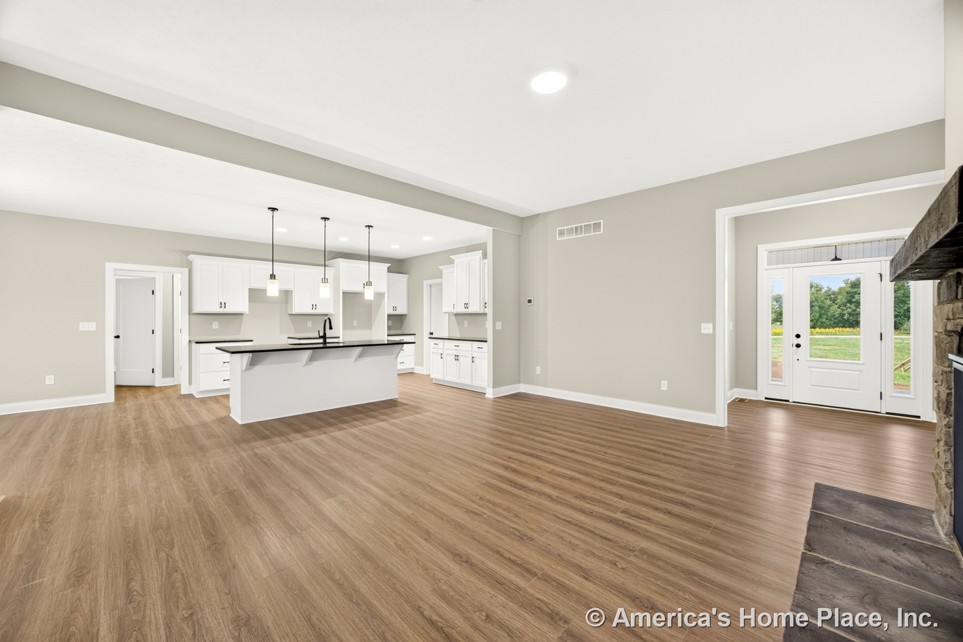 Open-concept living area with wood-look plank flooring, modern kitchen featuring white shaker cabinets, black solid surface countertops, kitchen island with pendant lighting, stone