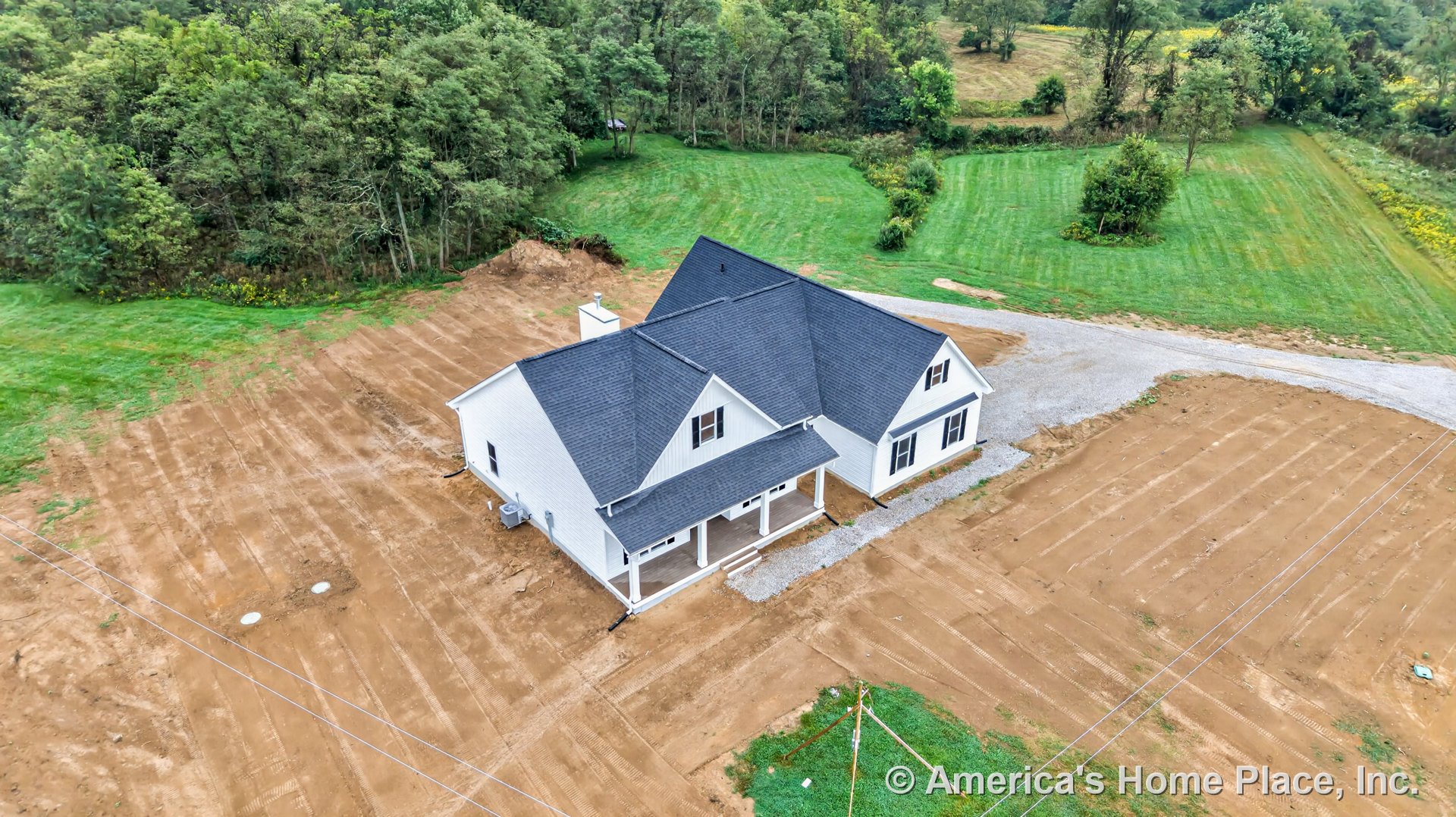 White siding exterior with black shingle roof, multiple gables, covered front porch supported by columns, double-hung windows, and gravel driveway in a rural setting.