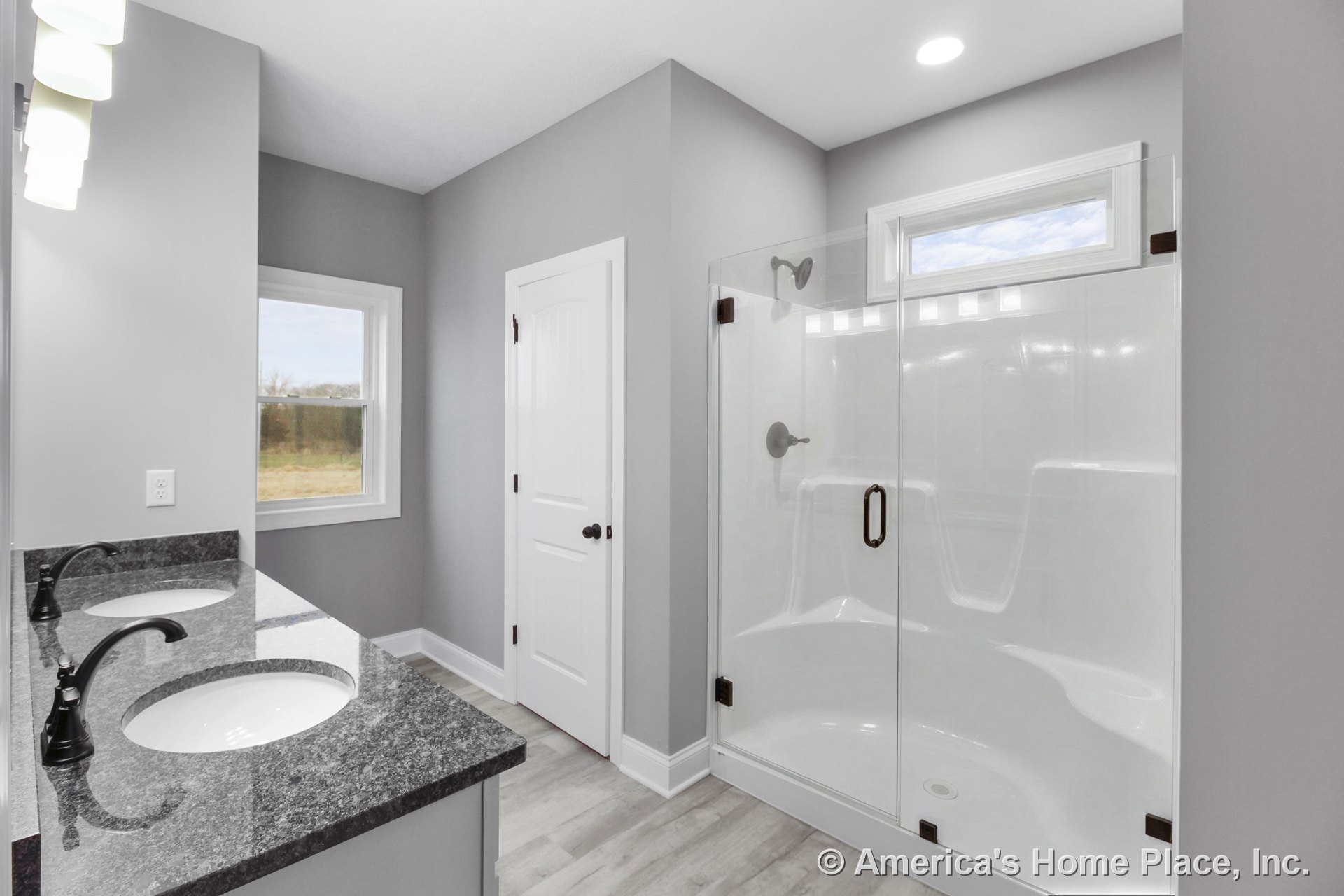 Double vanity with granite countertops and dual sinks, large glass-enclosed shower, gray painted walls with white trim and door, recessed ceiling lighting, and tile flooring.