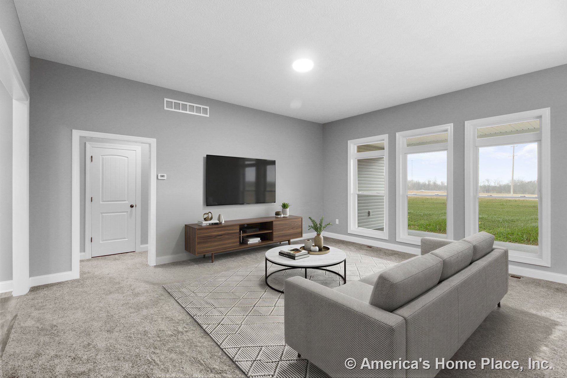 Living room with three large windows framed by white trim, gray carpet flooring, white paneled interior door, recessed ceiling light, gray painted walls, and wide white baseboard