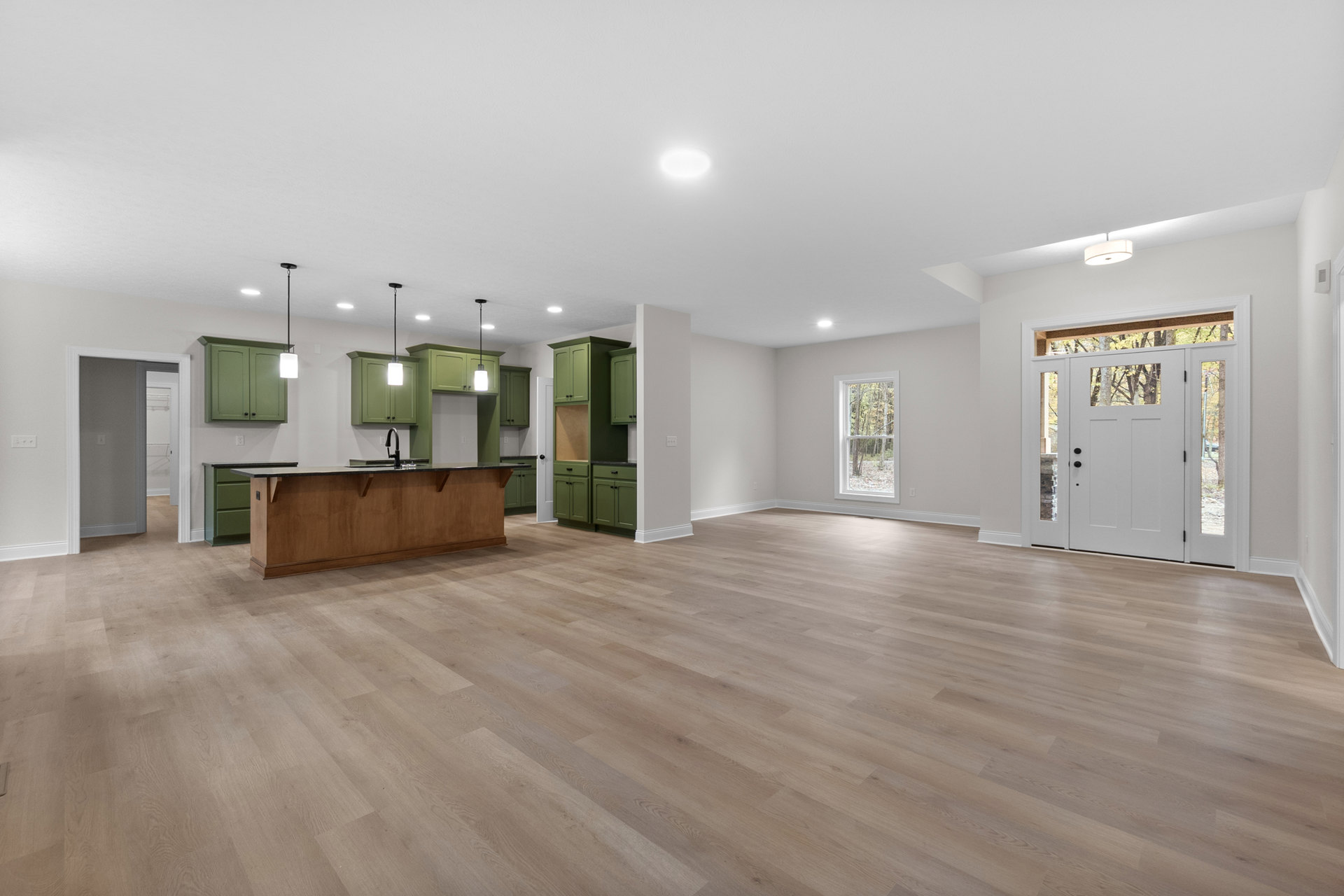 Spacious room with green cabinetry, wood flooring, white walls, large window showing trees, and a white door with glass panes