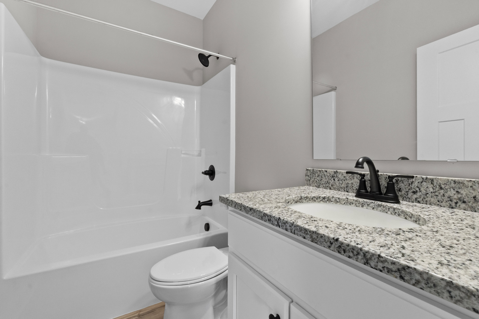 Marble countertop with black faucet, white sink, and toilet; tiled shower enclosure visible in modern bathroom