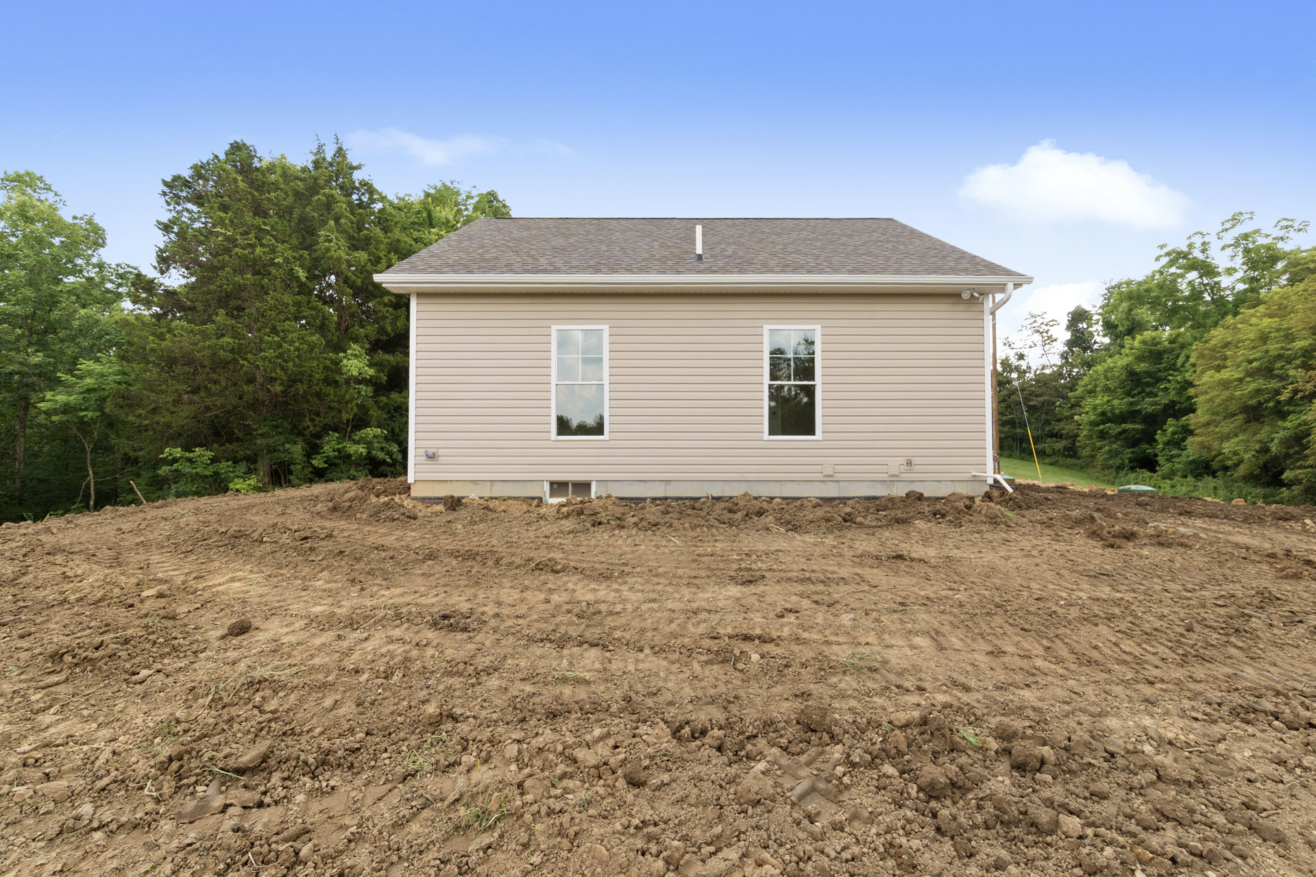 White-framed windows and chimney on a partially constructed house beside a dirt field, with trees and blue sky in the background