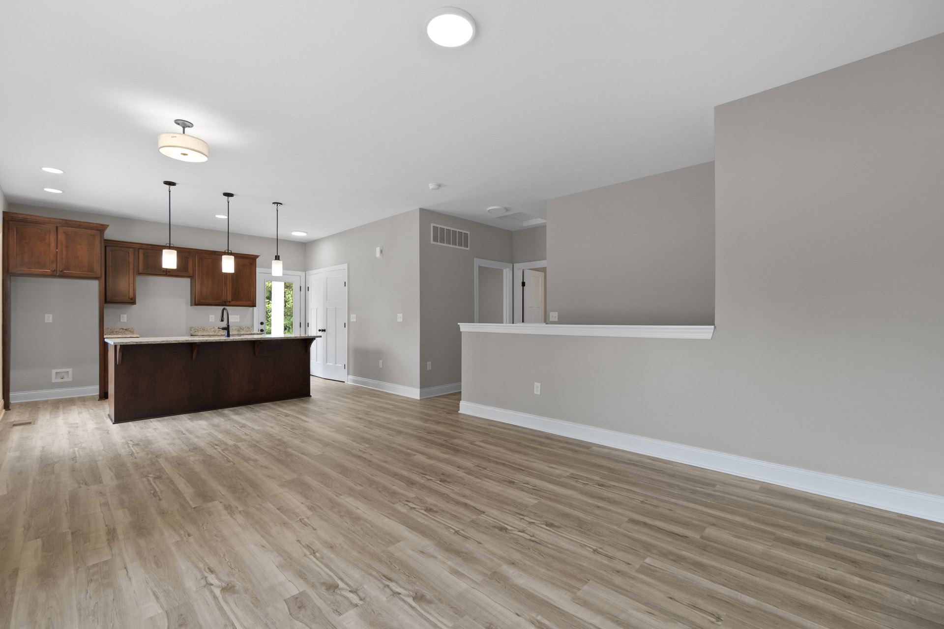 Open kitchen and dining area with wood flooring, white ceiling light fixture, light cabinetry, and a sink set into a spacious countertop.