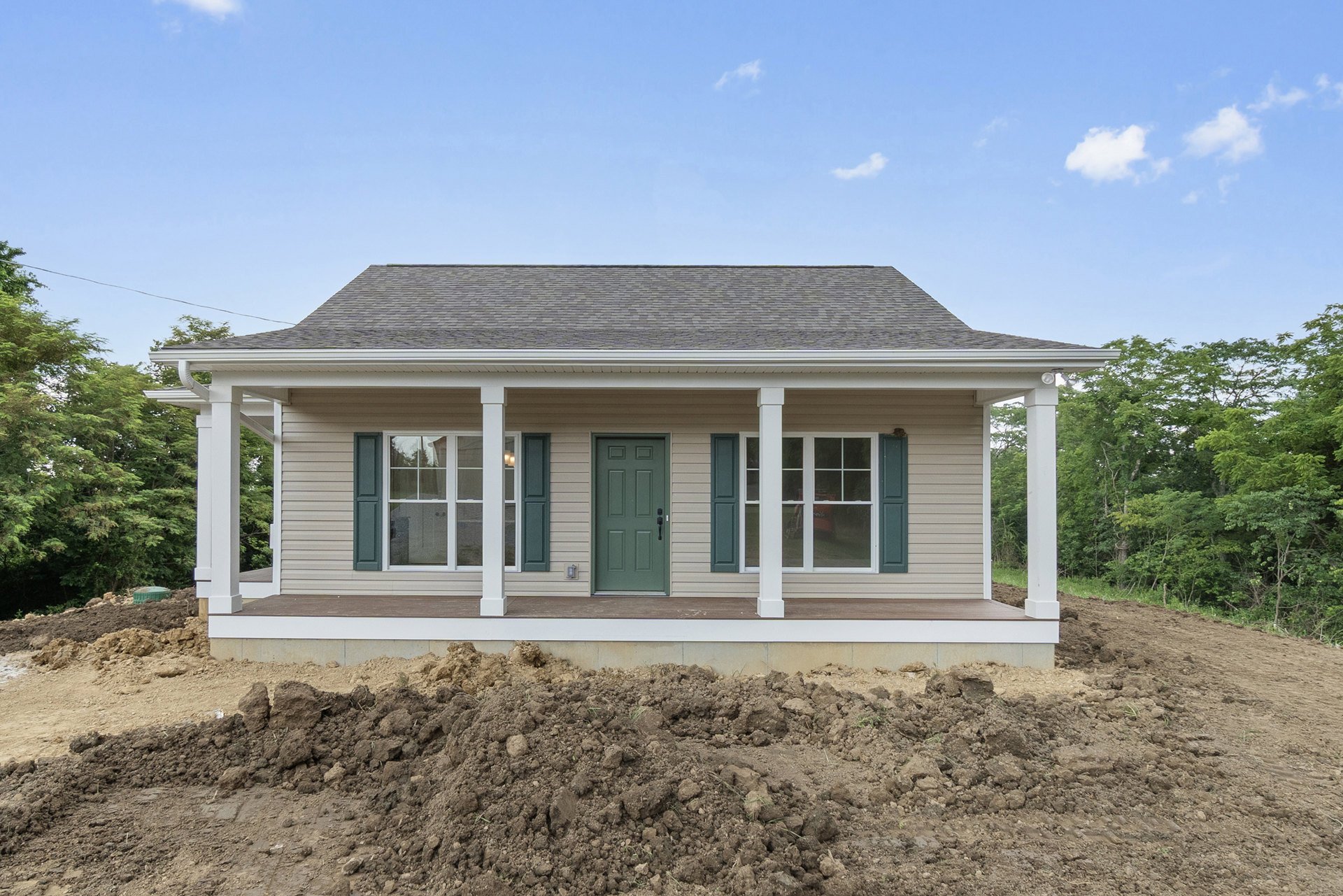 Two-story house with green front door, black handle, white-framed windows, gray roof, and a large pile of dirt beside the porch