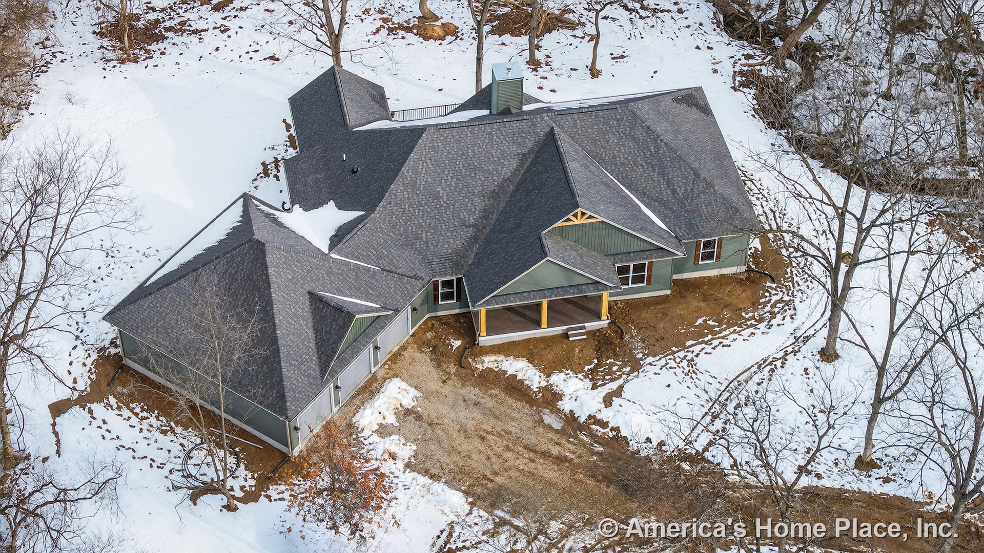 Aerial view of single-story home featuring dark shingle gabled roof, covered front entry porch, green siding exterior with white trim windows, and unfinished driveway.