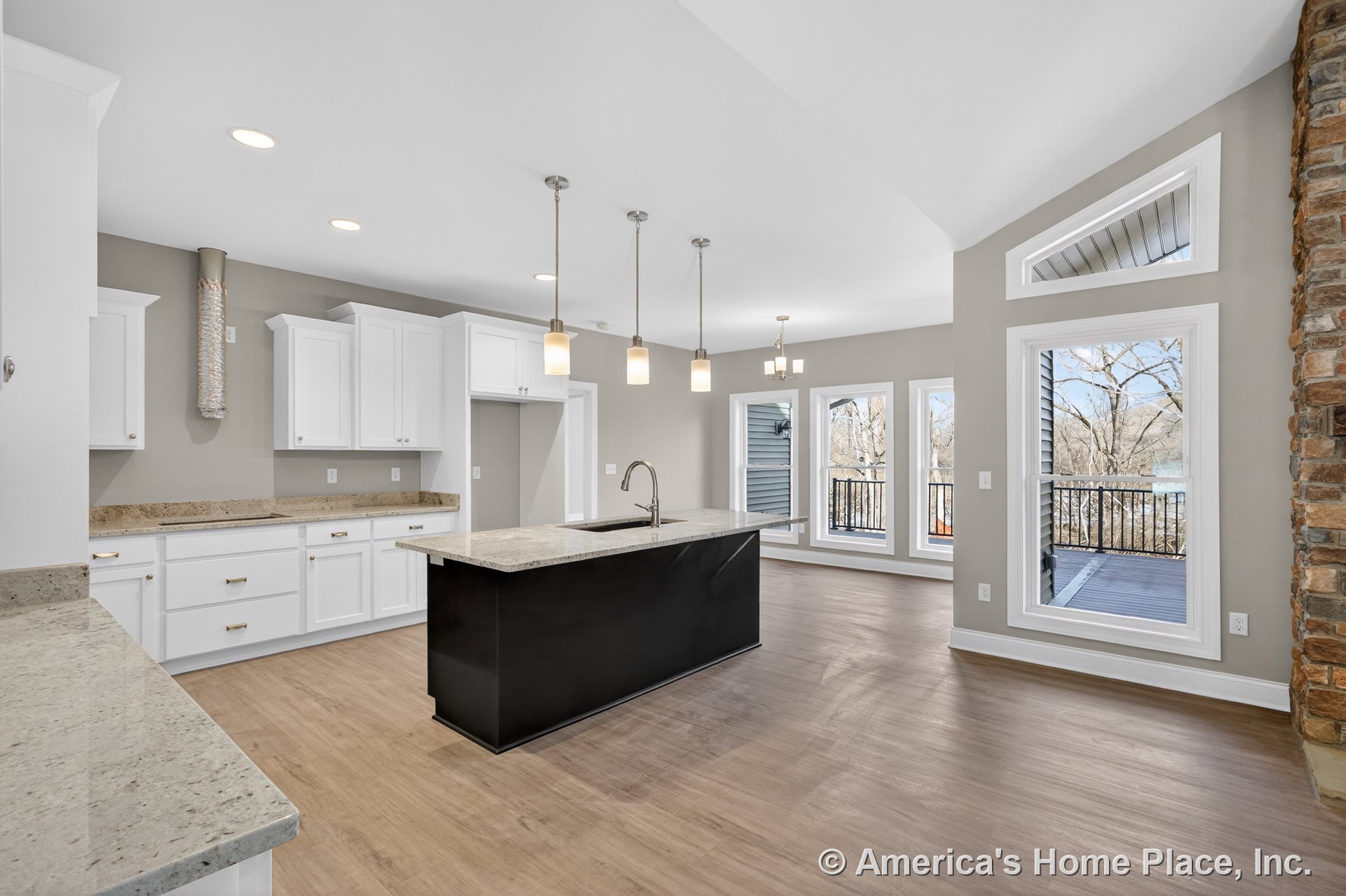 White kitchen with upper and lower cabinets, stone countertops, central island with sink, pendant and recessed lighting, wood-look flooring, large windows with trim overlooking