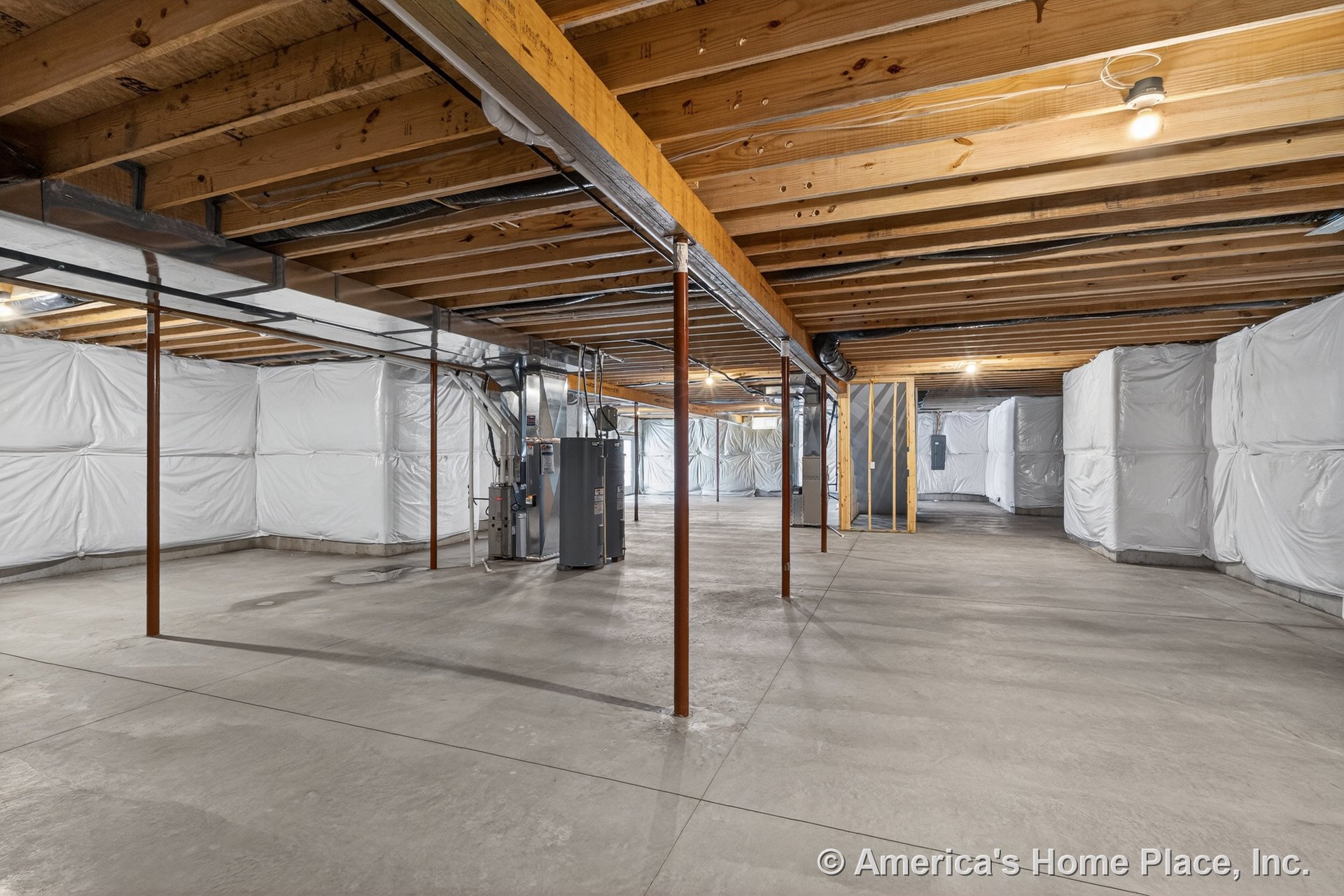 Unfinished basement with exposed wood ceiling joists, concrete slab floor, insulated wall panels, metal support columns, utility area housing HVAC equipment, bare light fixtures