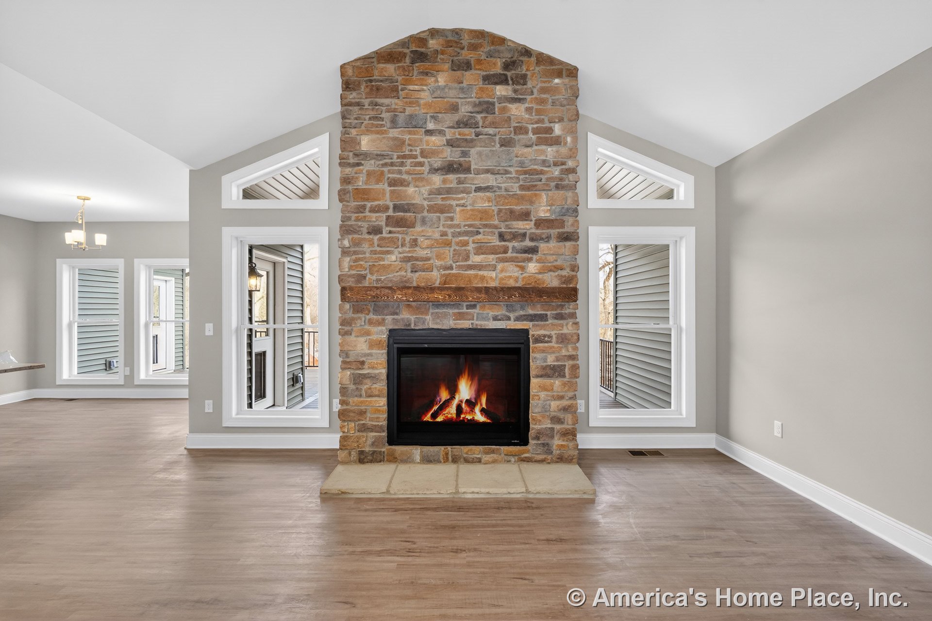 Floor-to-ceiling stone fireplace with wood mantel, expansive windows, vaulted ceiling, light wood flooring, and neutral walls showcasing modern finishes and abundant natural light.