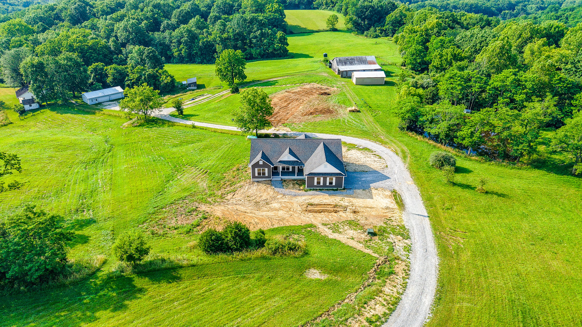 White two-story house with attached garage, gray shingle roof, surrounded by mature trees and green lawn