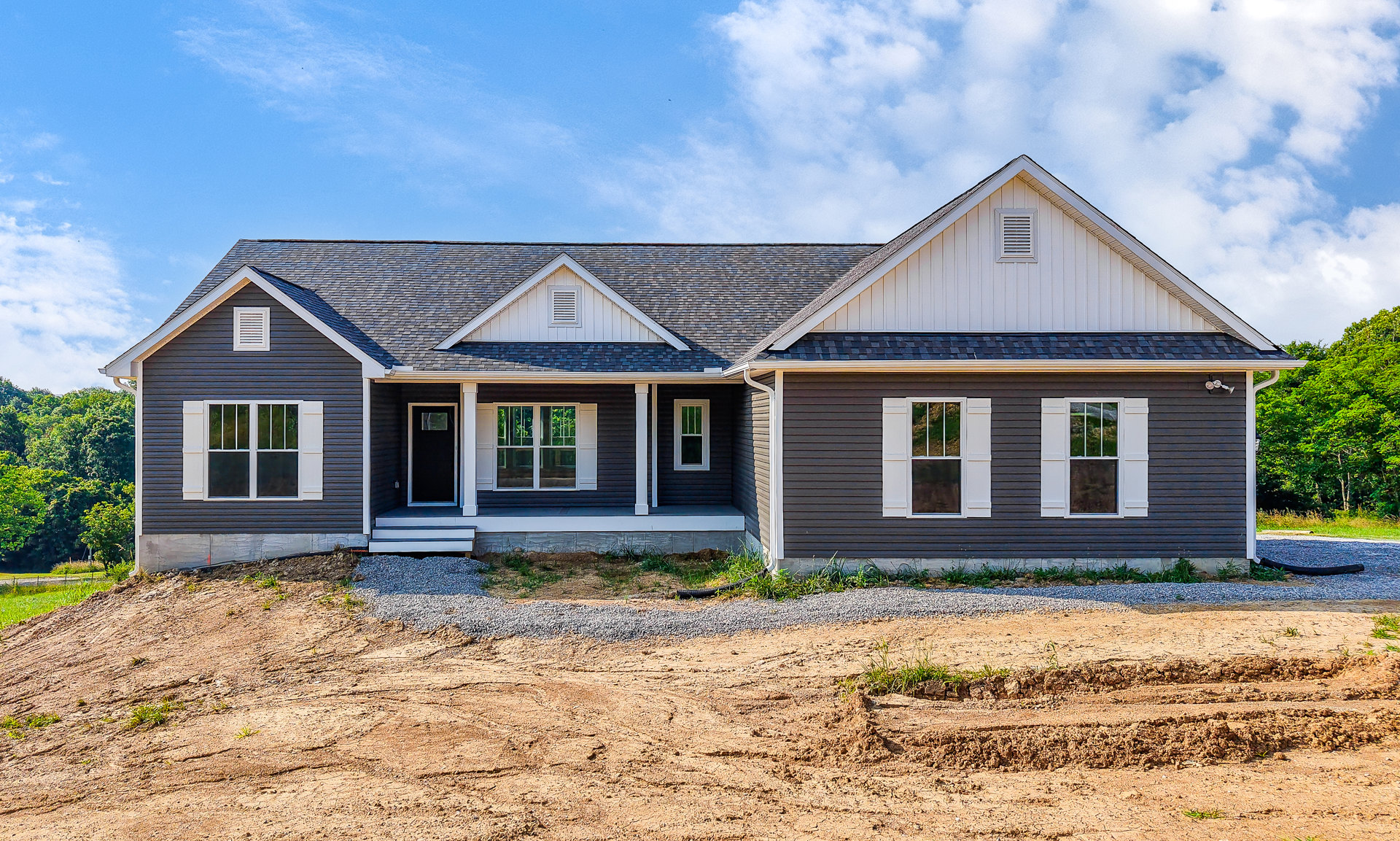 Two-story brick house with black front door, white-trimmed windows, and dirt patch yard under cloudy sky
