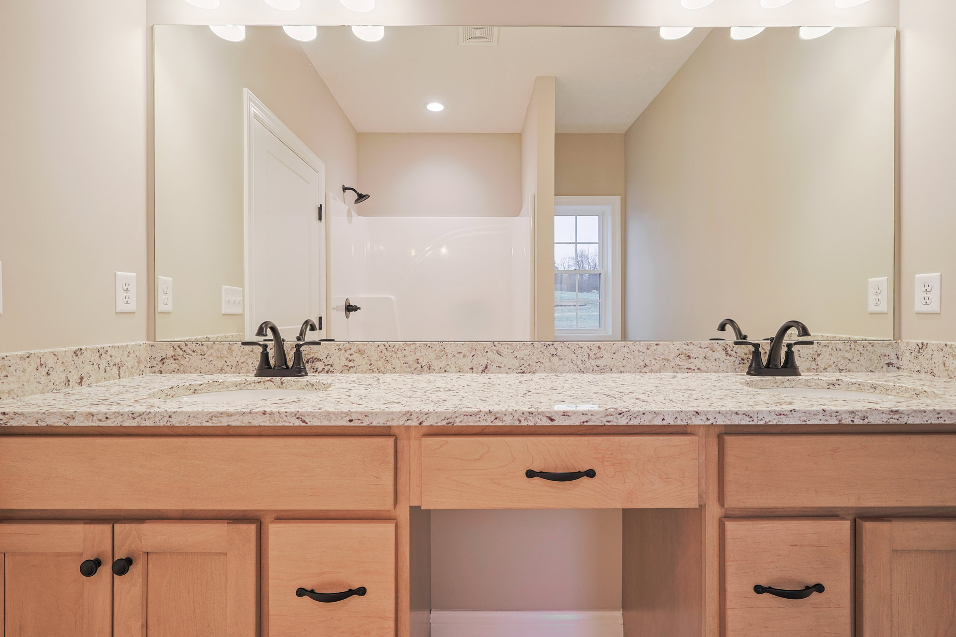 Bathroom with marble countertop, white cabinetry and drawers, wall-mounted mirror, electrical outlet, window overlooking trees, white door with black hinge, tile flooring