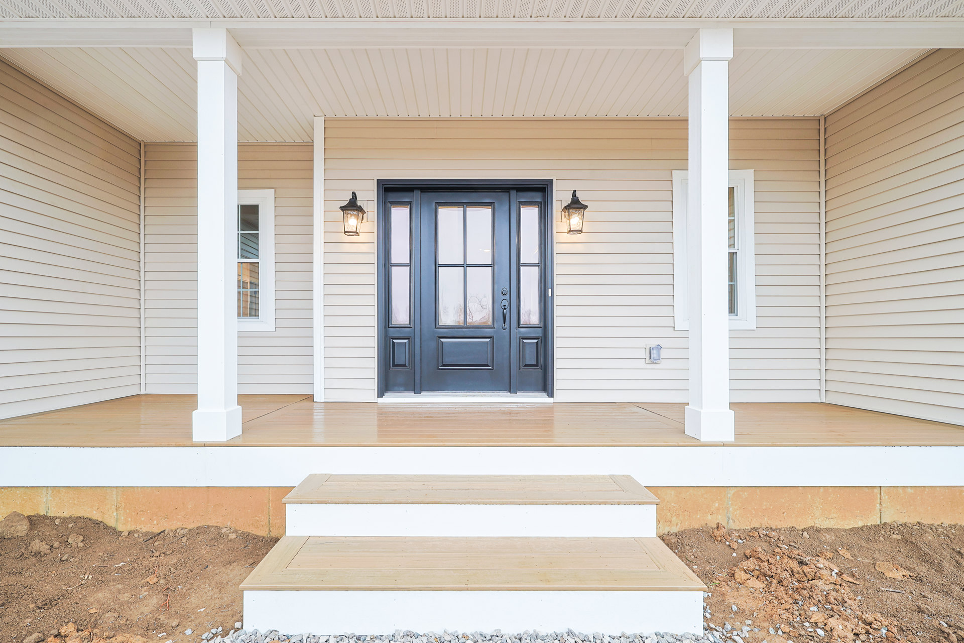 Blue front door with glass panes set in white siding, wood plank porch, adjacent window with white frame and glass panel