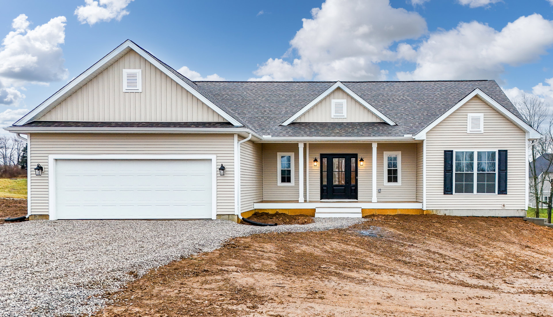 Two-story house with white siding, black front door with glass panes, multi-pane window, attached white garage door, paved driveway, and white wall vent under a cloudy sky