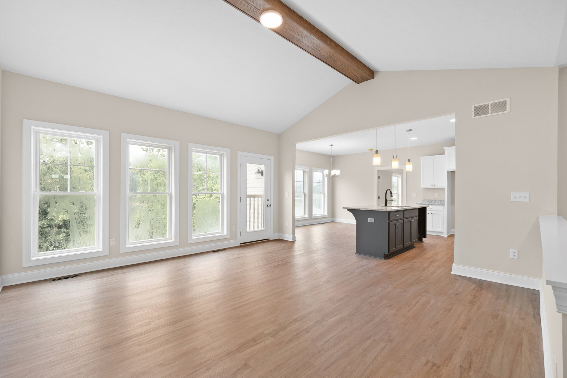 Spacious open floor plan featuring hardwood flooring, central kitchen island with sink, white-framed windows including frosted glass, wall vent, and a fireplace set in the middle