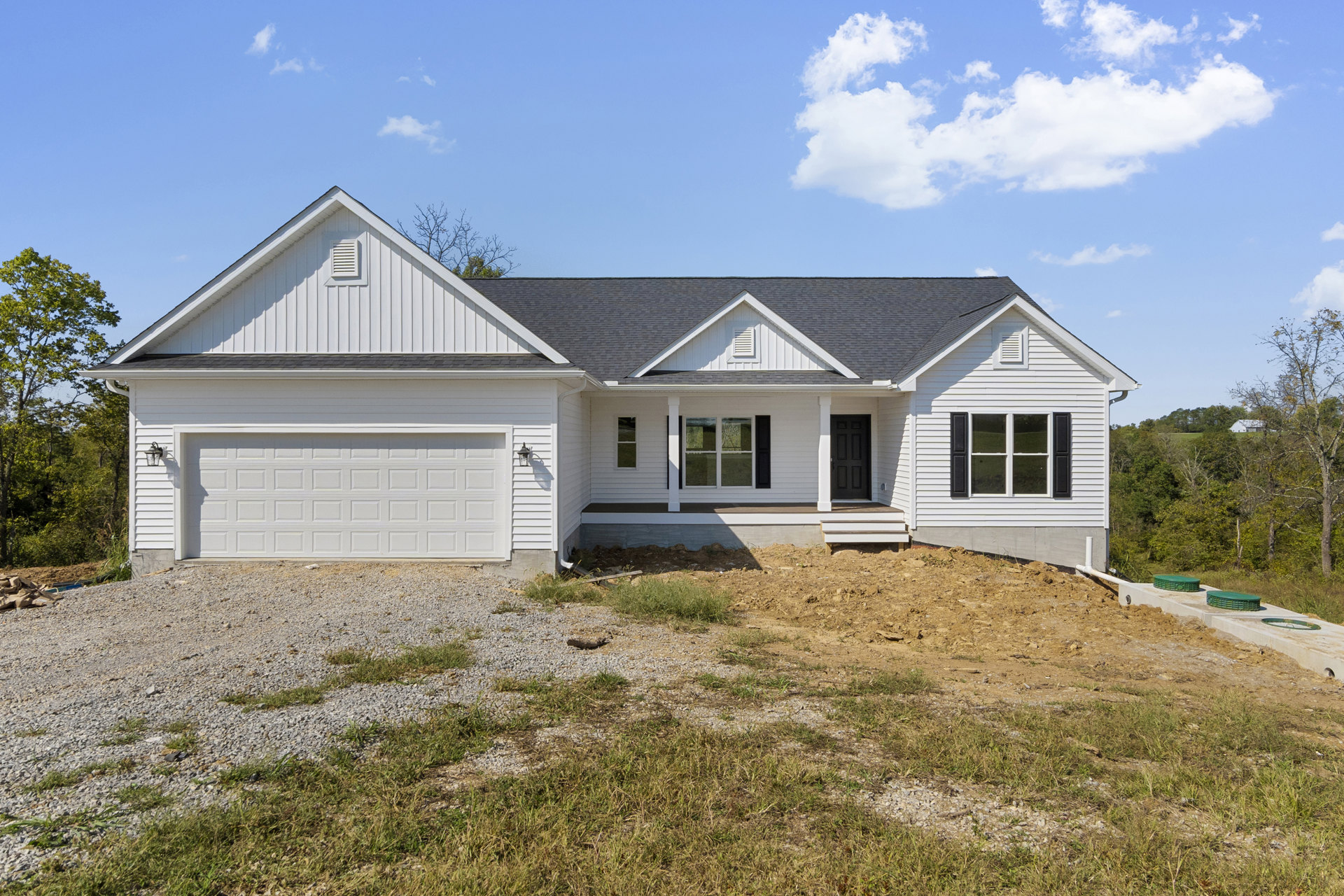White two-story house with black front door, attached garage, paved driveway, large windows, and mature trees in the background