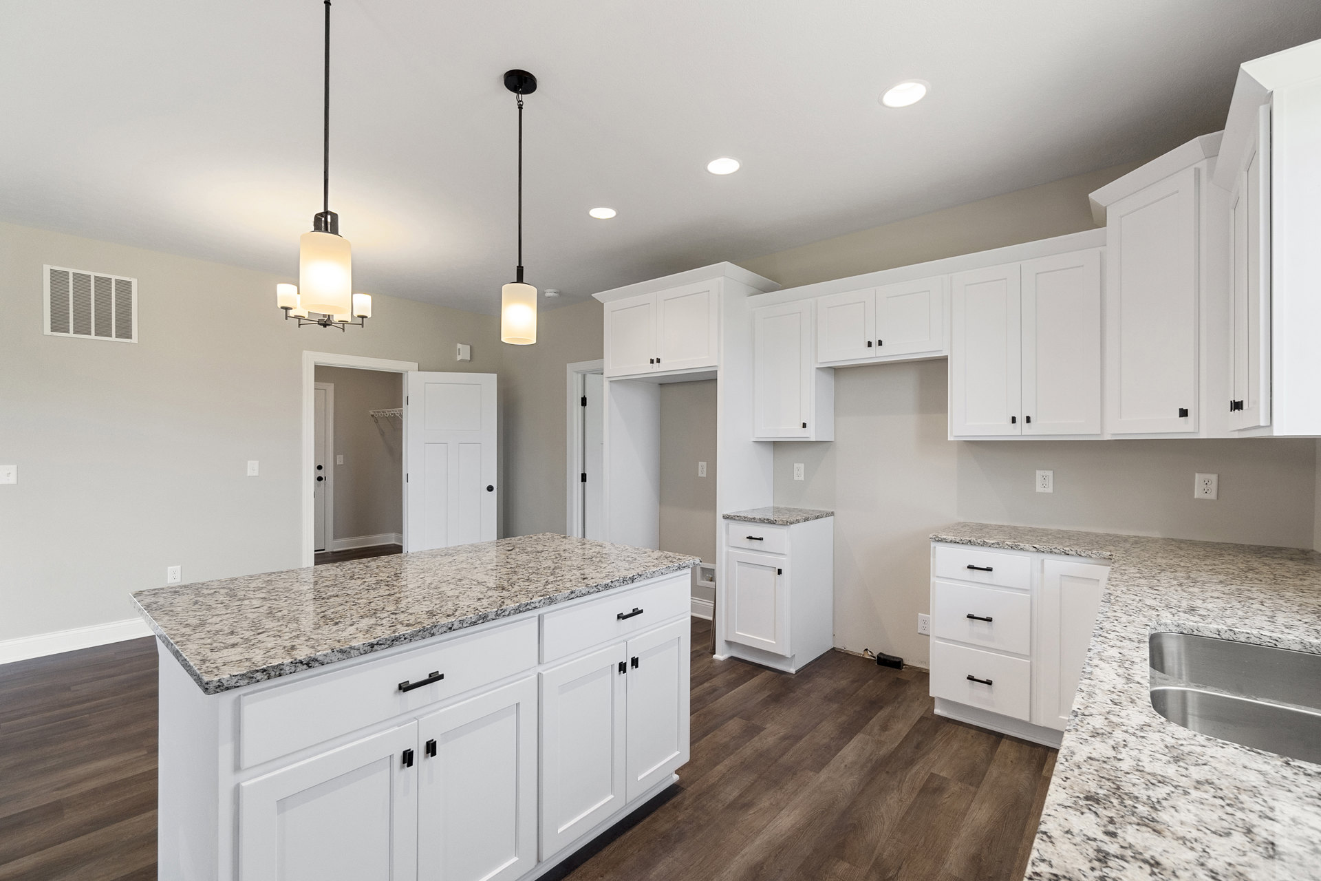White kitchen with marble countertops, white shaker cabinets with black handles, stainless steel sink, and light wood flooring