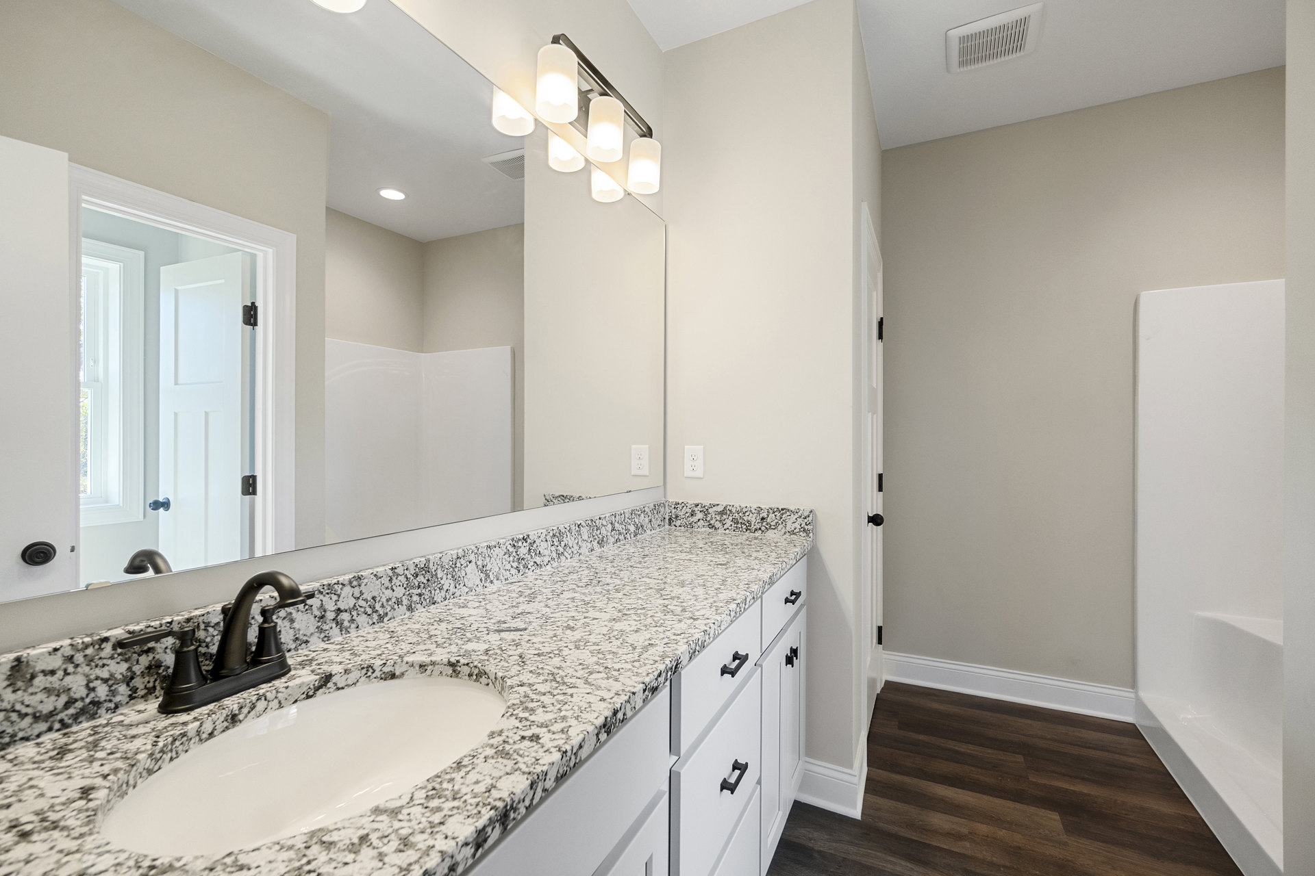 Marble countertop with undermount sink, matte black faucet, large mirror, white door with black hardware, ceiling vent, light tile flooring