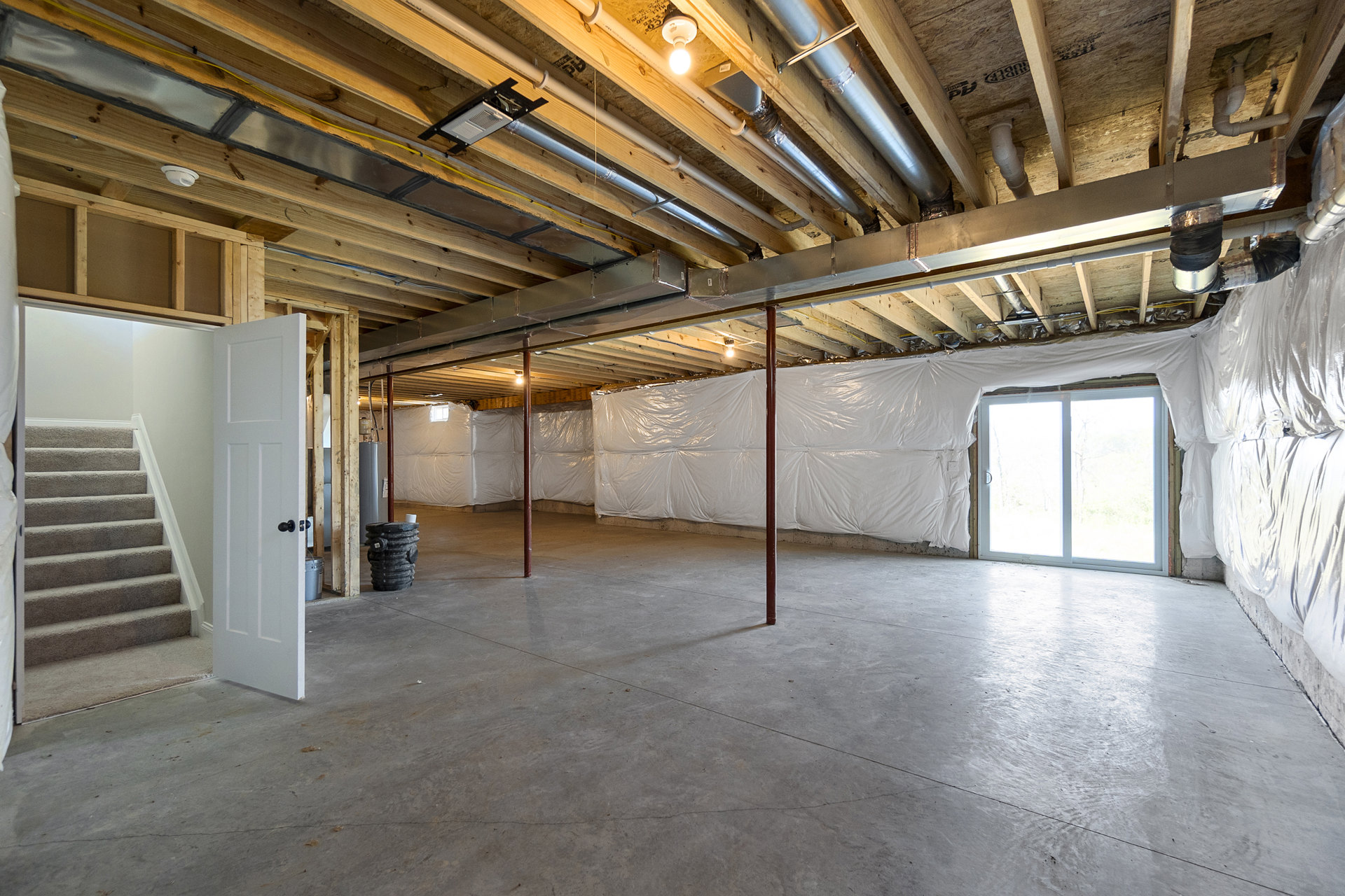 Modern room featuring a glass door and solid white door, light plaster walls, exposed ceiling beam, white curtain over window, and partial view of staircase with black and silver