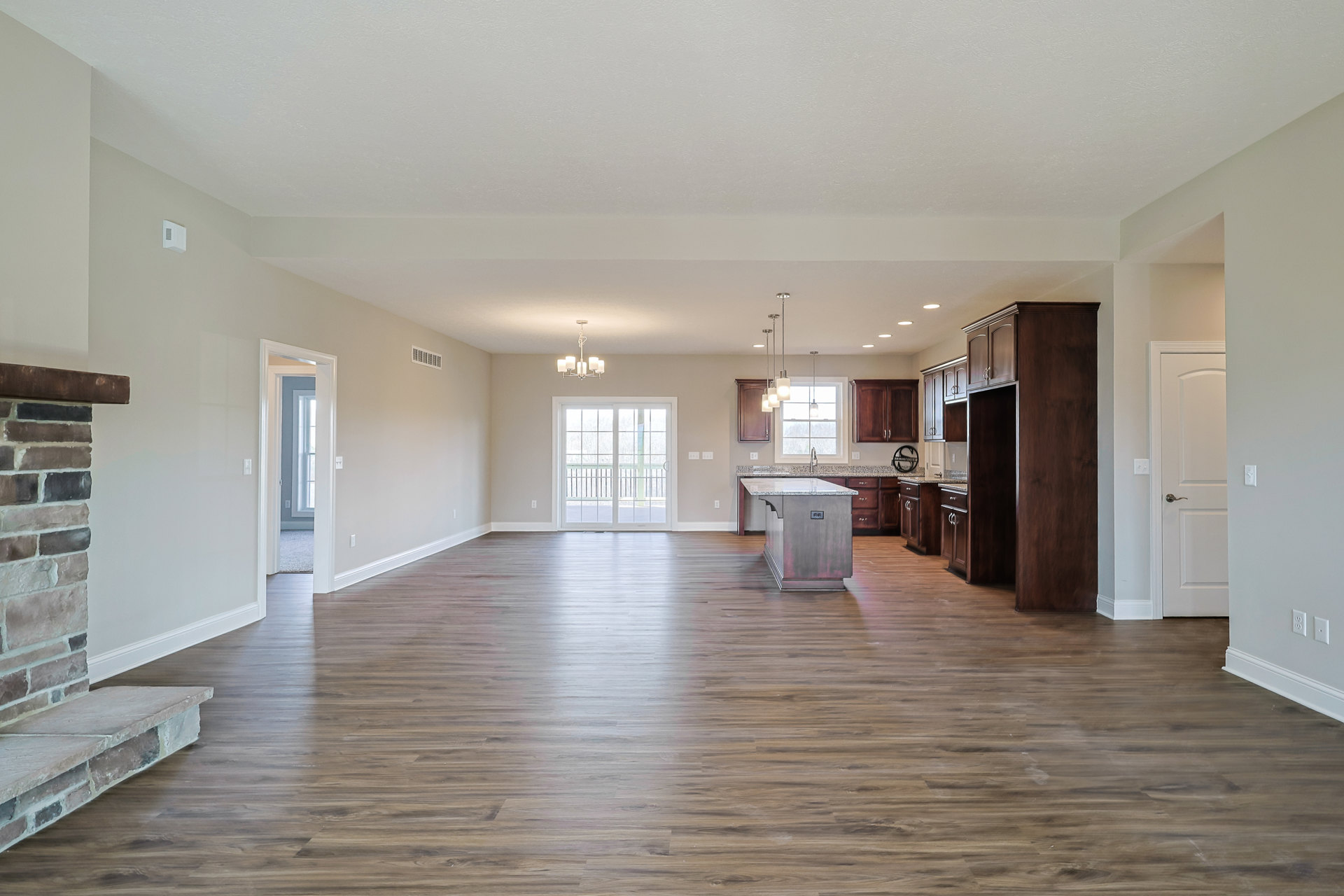 Spacious open floor plan featuring hardwood floors, a central kitchen island with marble countertops, brick fireplace set against a white wall, large windows with railing