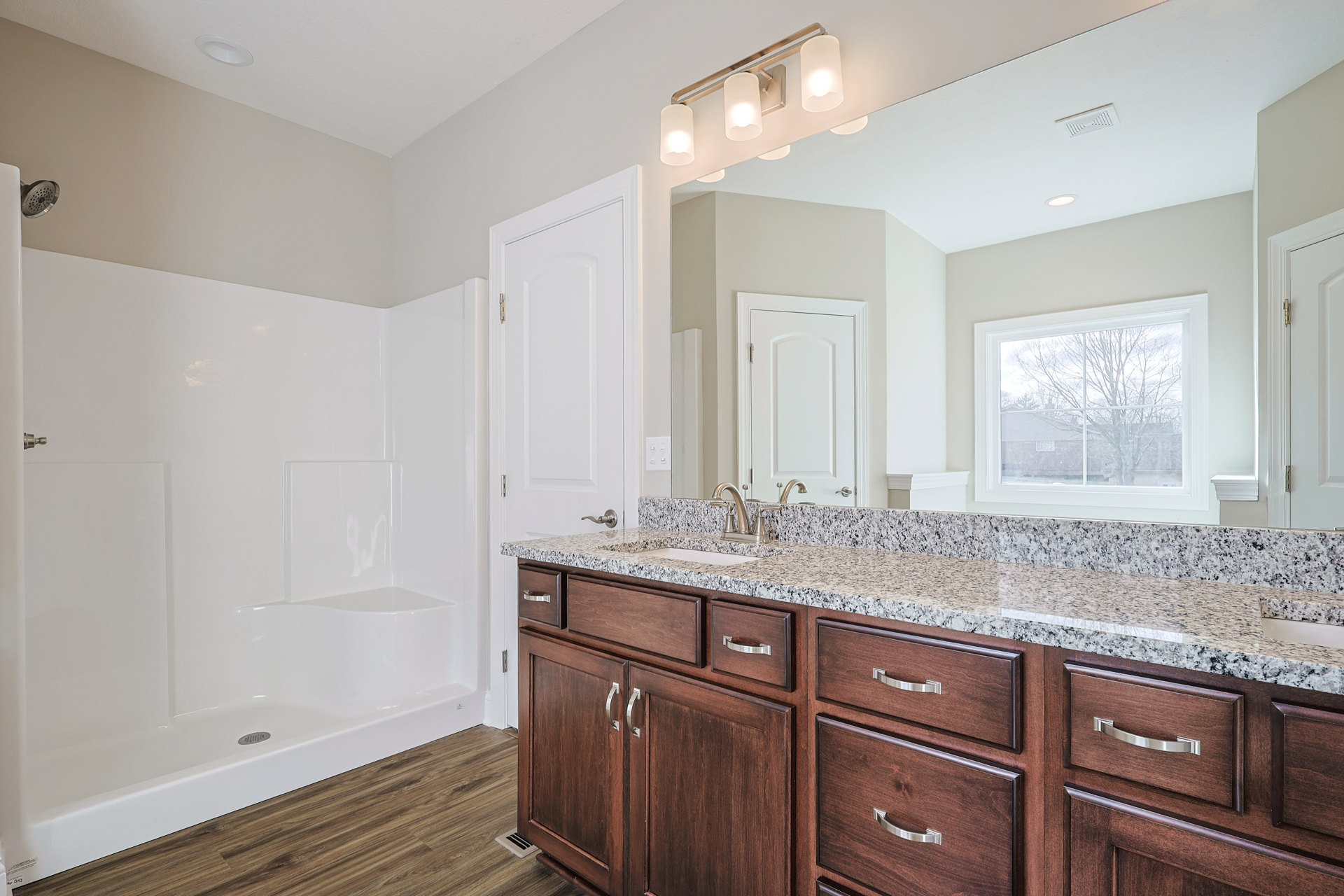 Bathroom featuring marble countertop with undermount sink, white cabinetry with drawers, freestanding bathtub near window overlooking tree, tiled shower area with modern shower
