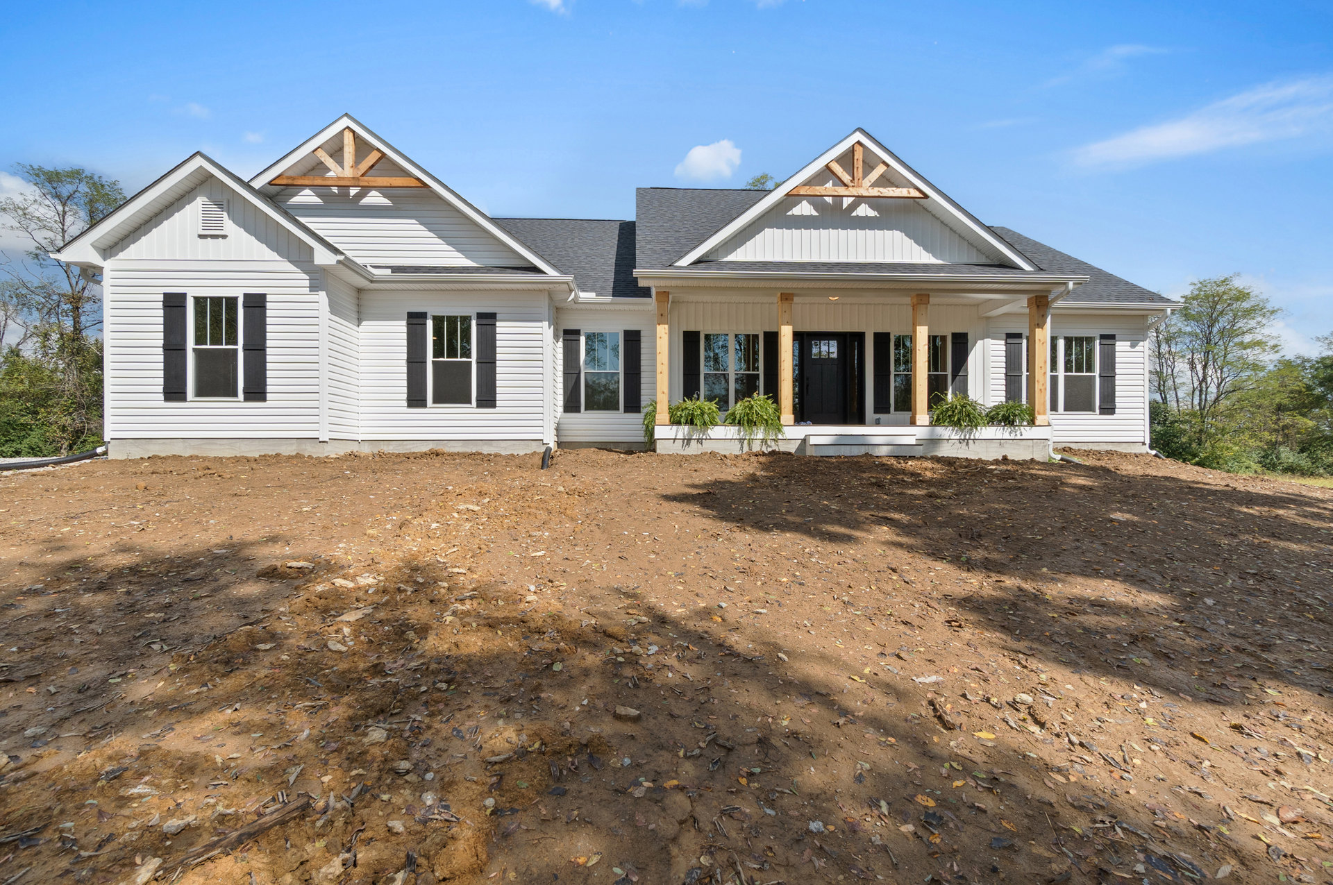 Two-story house with white-framed windows, black shutters, and a dirt yard scattered with leaves; small plant sits on a ledge near the entrance.
