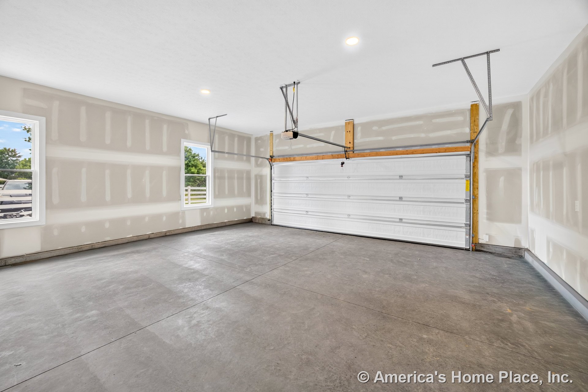 Garage with unfinished drywall walls, concrete slab flooring, double overhead door equipped with automatic opener, two exterior windows providing natural light, recessed ceiling