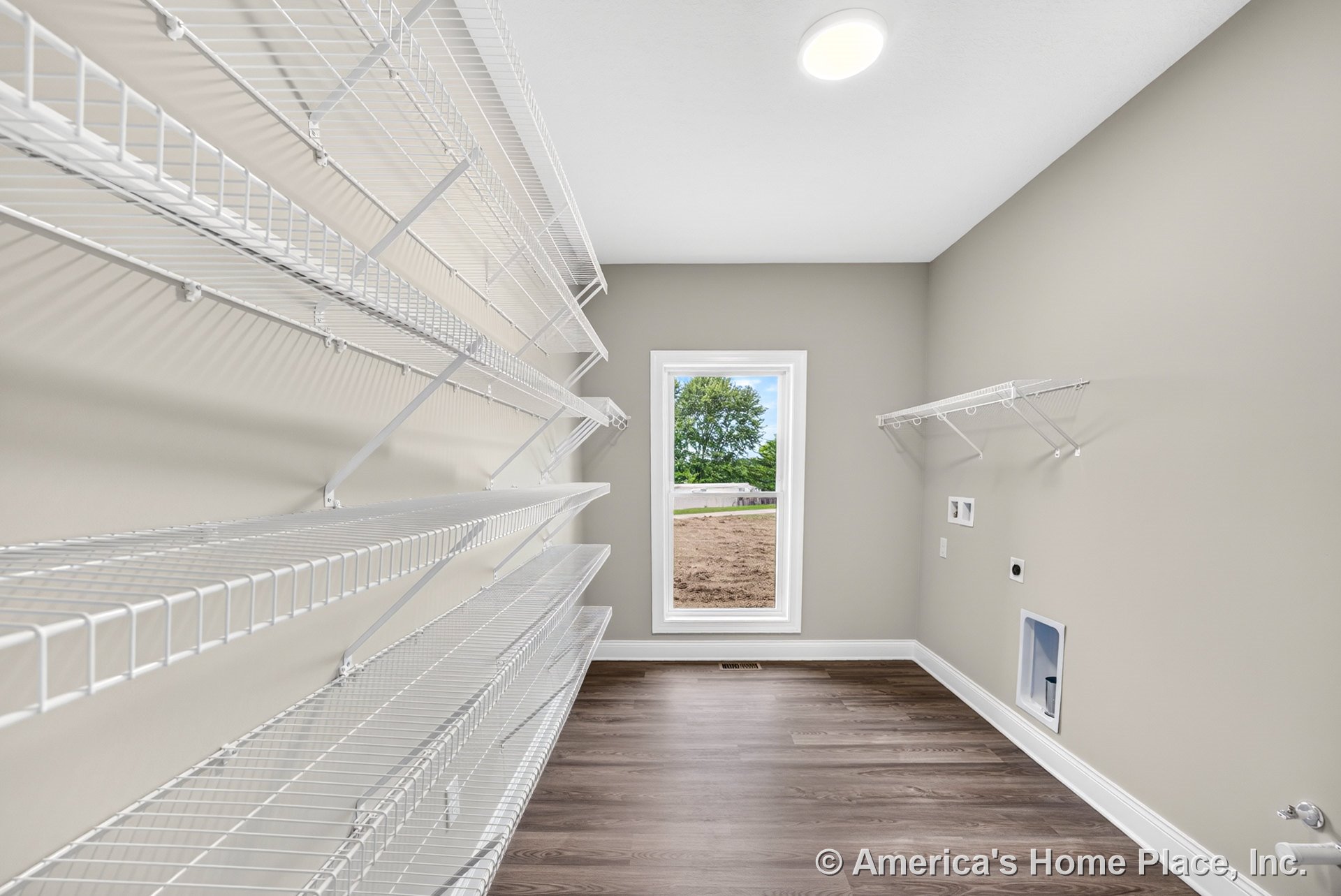 Utility pantry with built-in white wire shelving, laundry hookups, large window, vinyl plank flooring, neutral walls, baseboard trim, and recessed ceiling lighting.