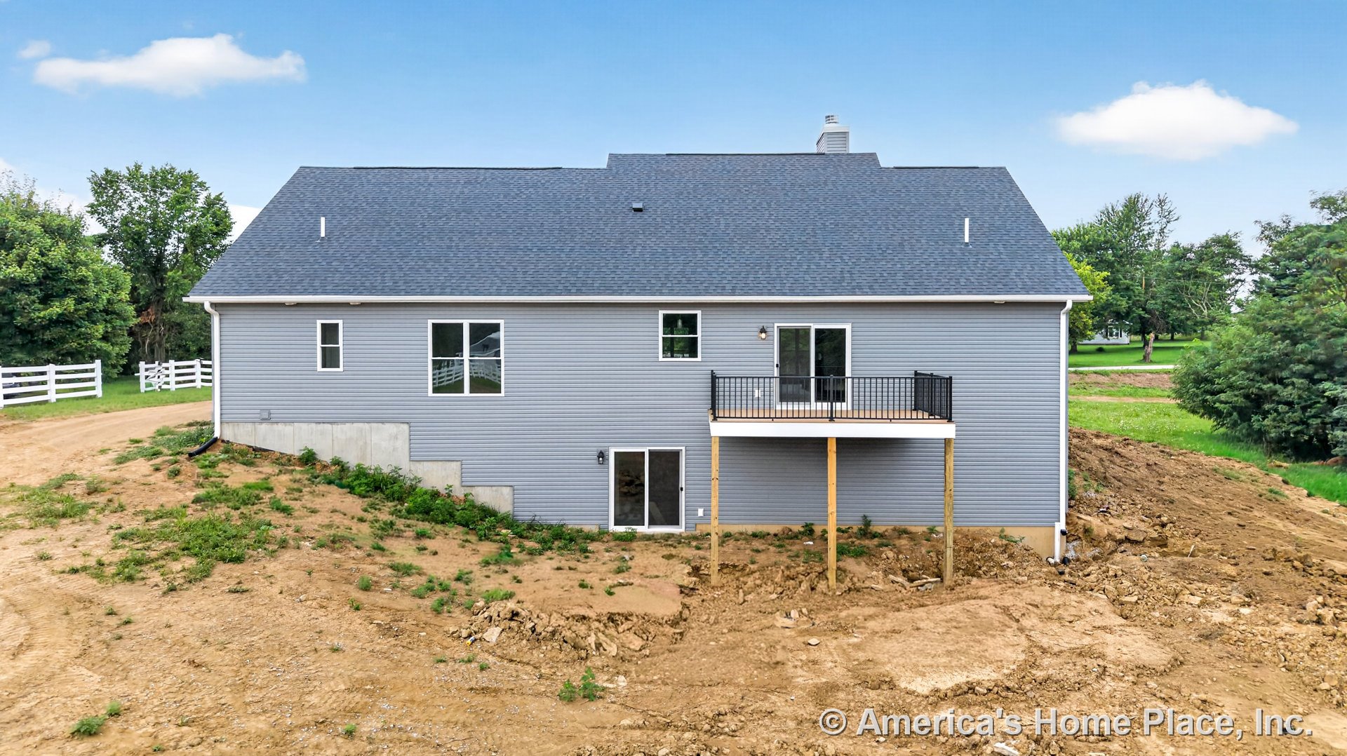 Gray vinyl siding exterior with multiple windows, walk-out basement, elevated deck featuring black metal railing, sliding doors, asphalt shingle roof, white trim, exposed