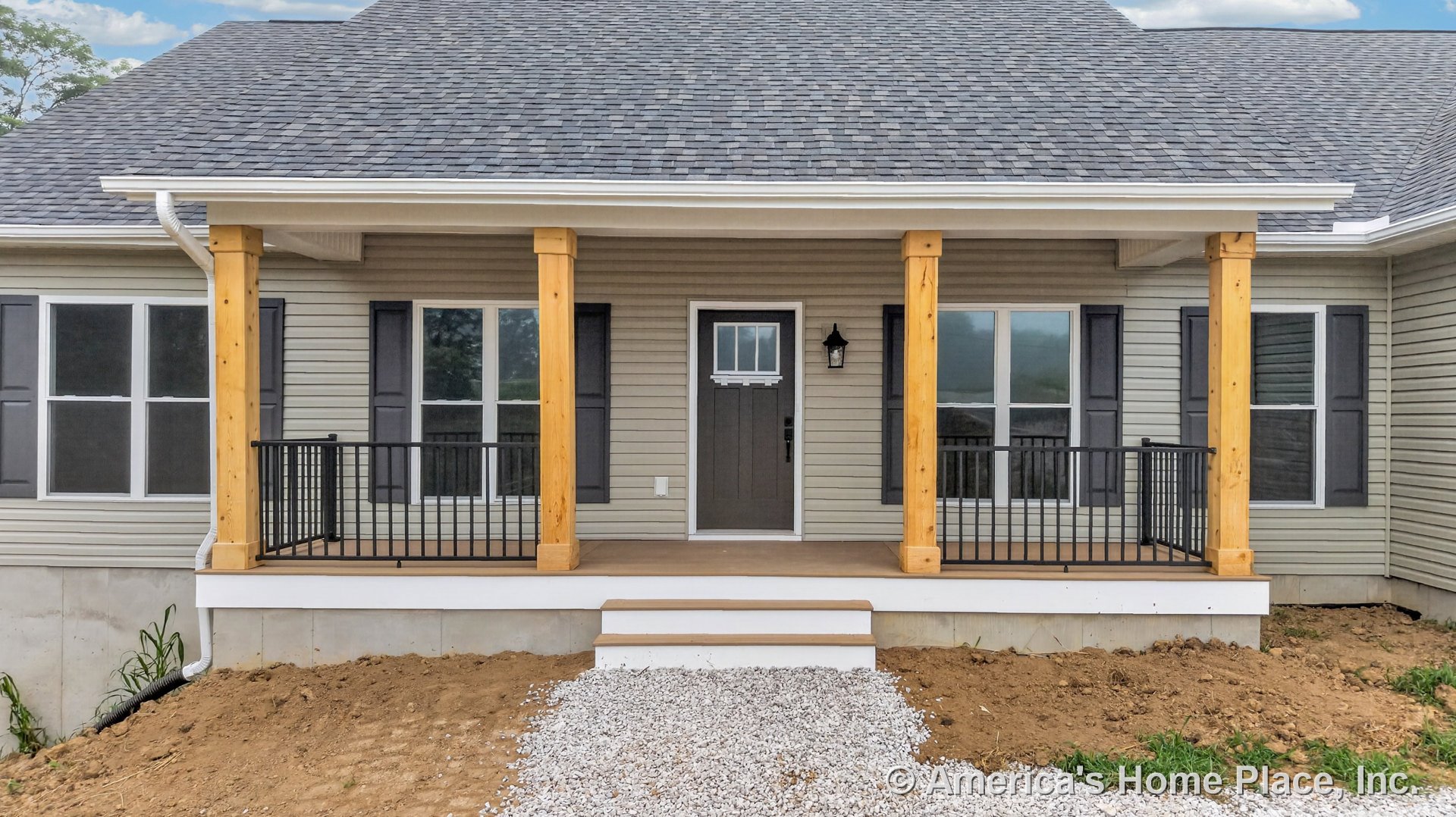 Covered front porch with natural wood support columns, black metal railings, gray shingle roof, double front windows with shutters, single entry door topped by a transom window